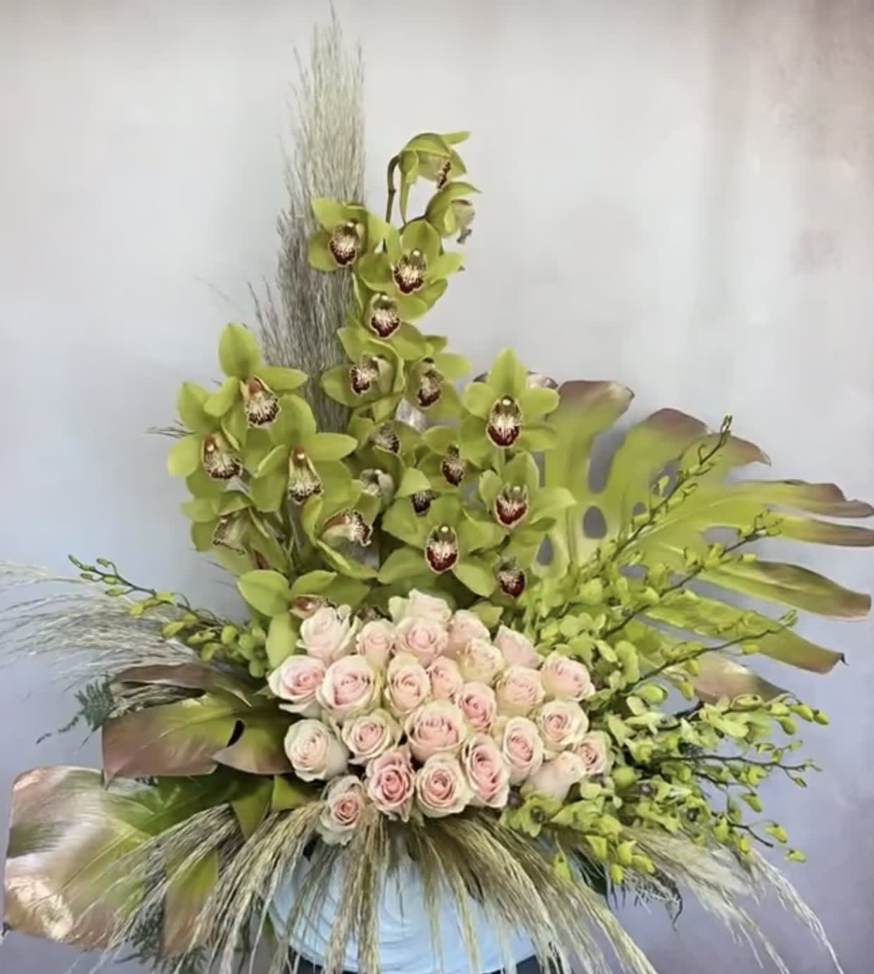 Tall floral arrangement with pale pink roses and green orchids in a vase