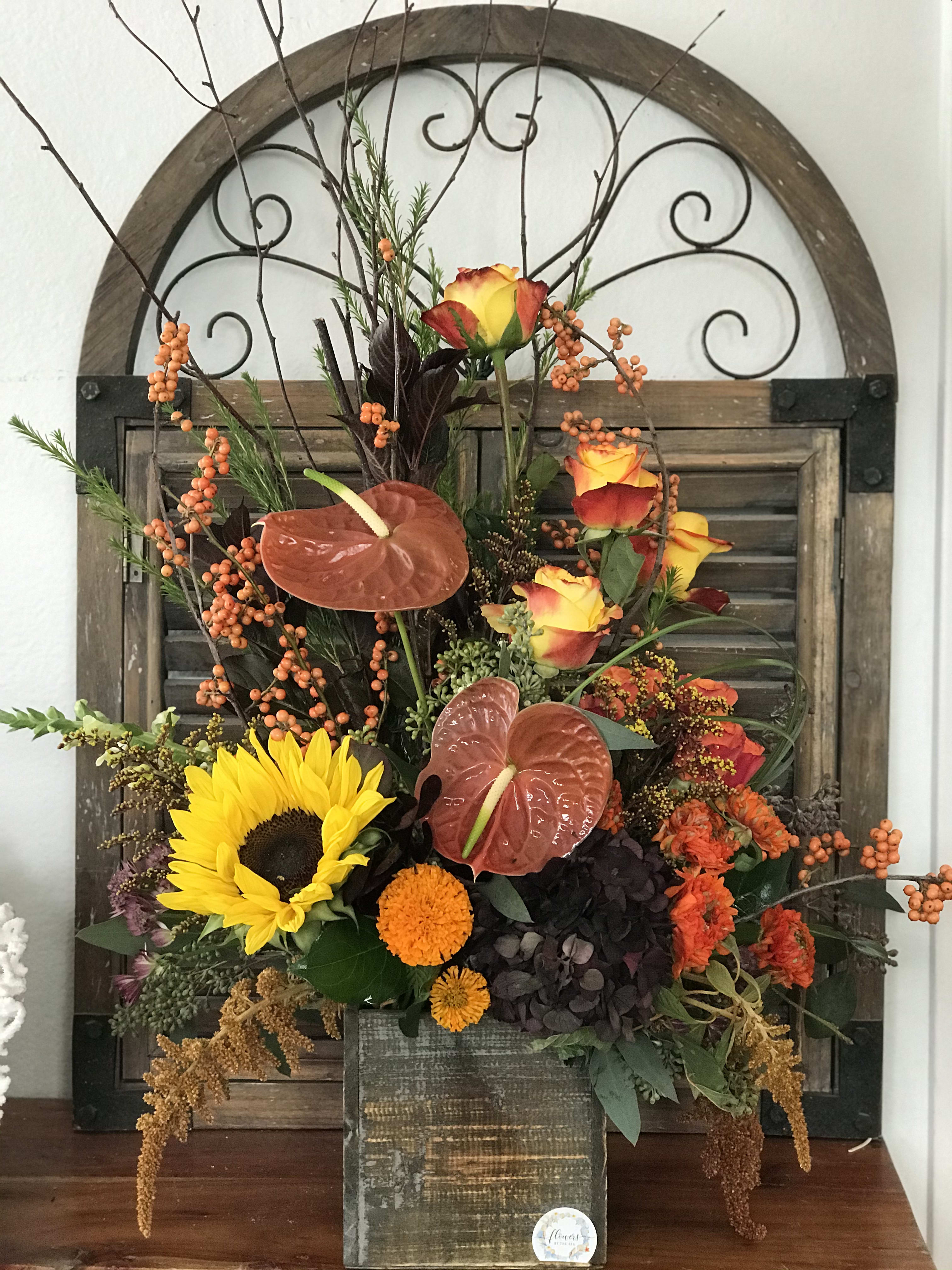 Mixed autumn floral arrangement with sunflowers, roses, and anthuriums in a wooden container