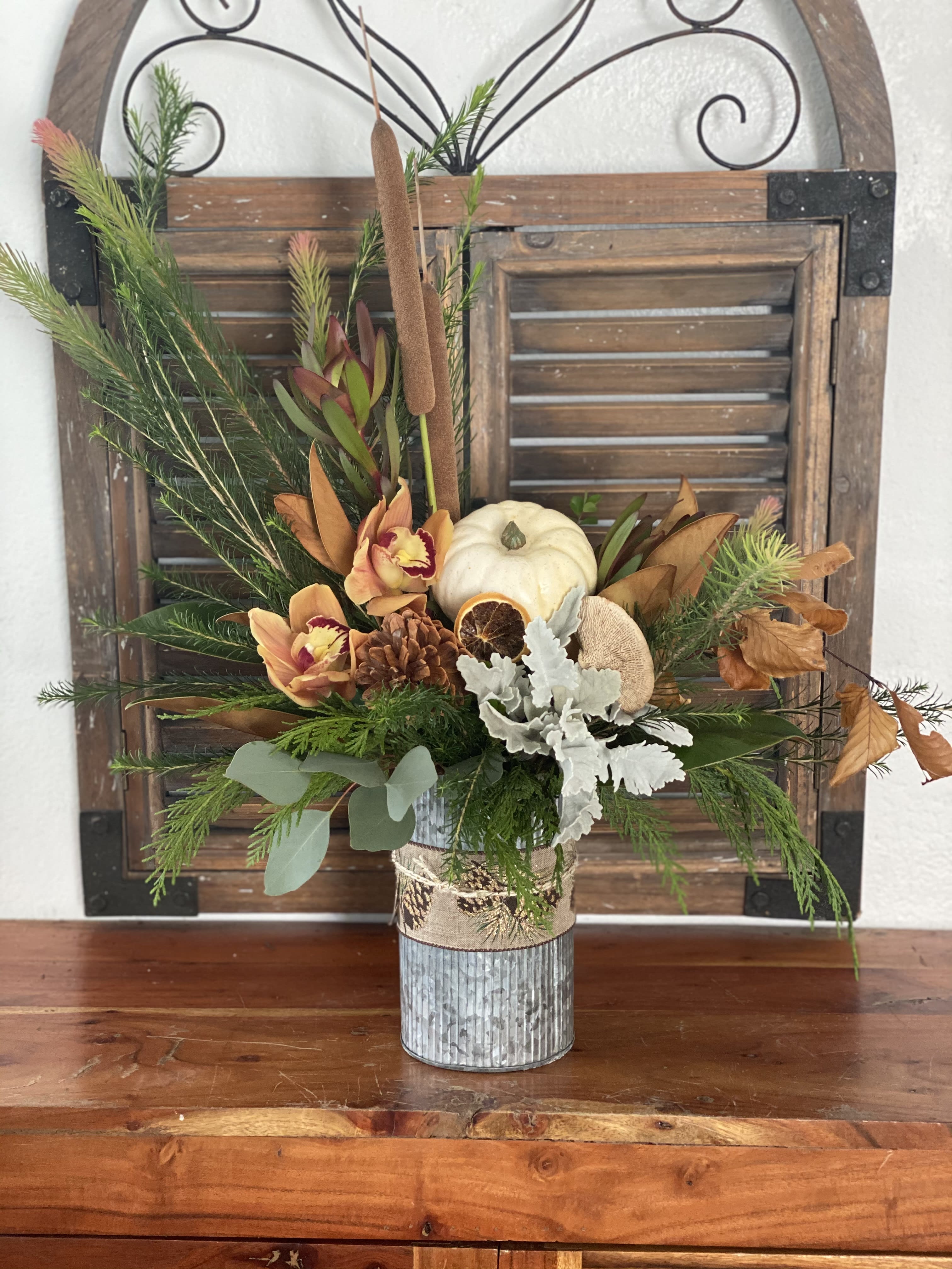 Autumn floral arrangement in a metal vase with a white pumpkin and dried accents