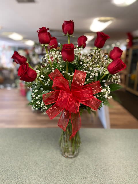 Red roses in a glass vase with baby's breath and a red bow