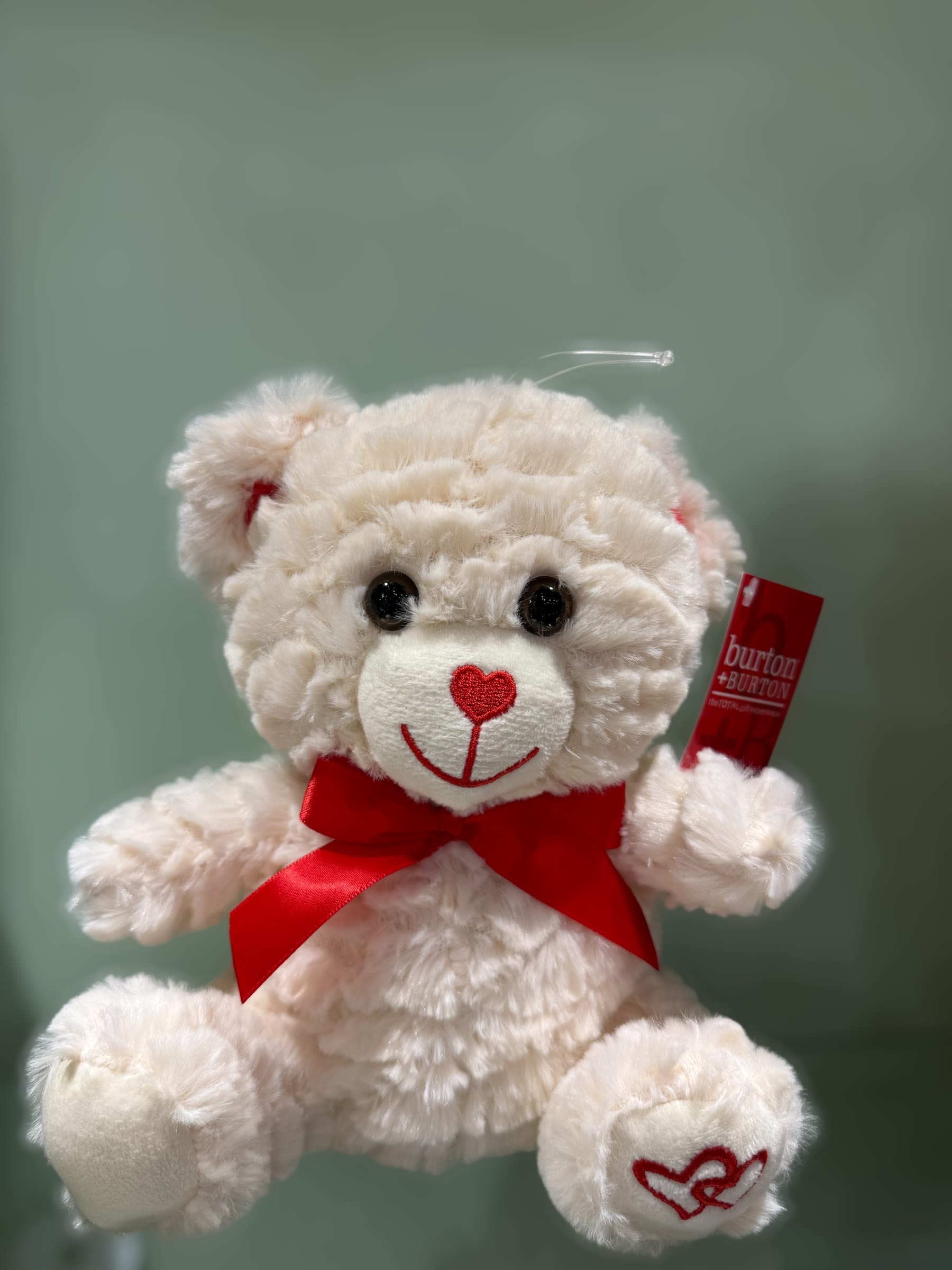 Cream plush teddy bear with a red bow and heart nose