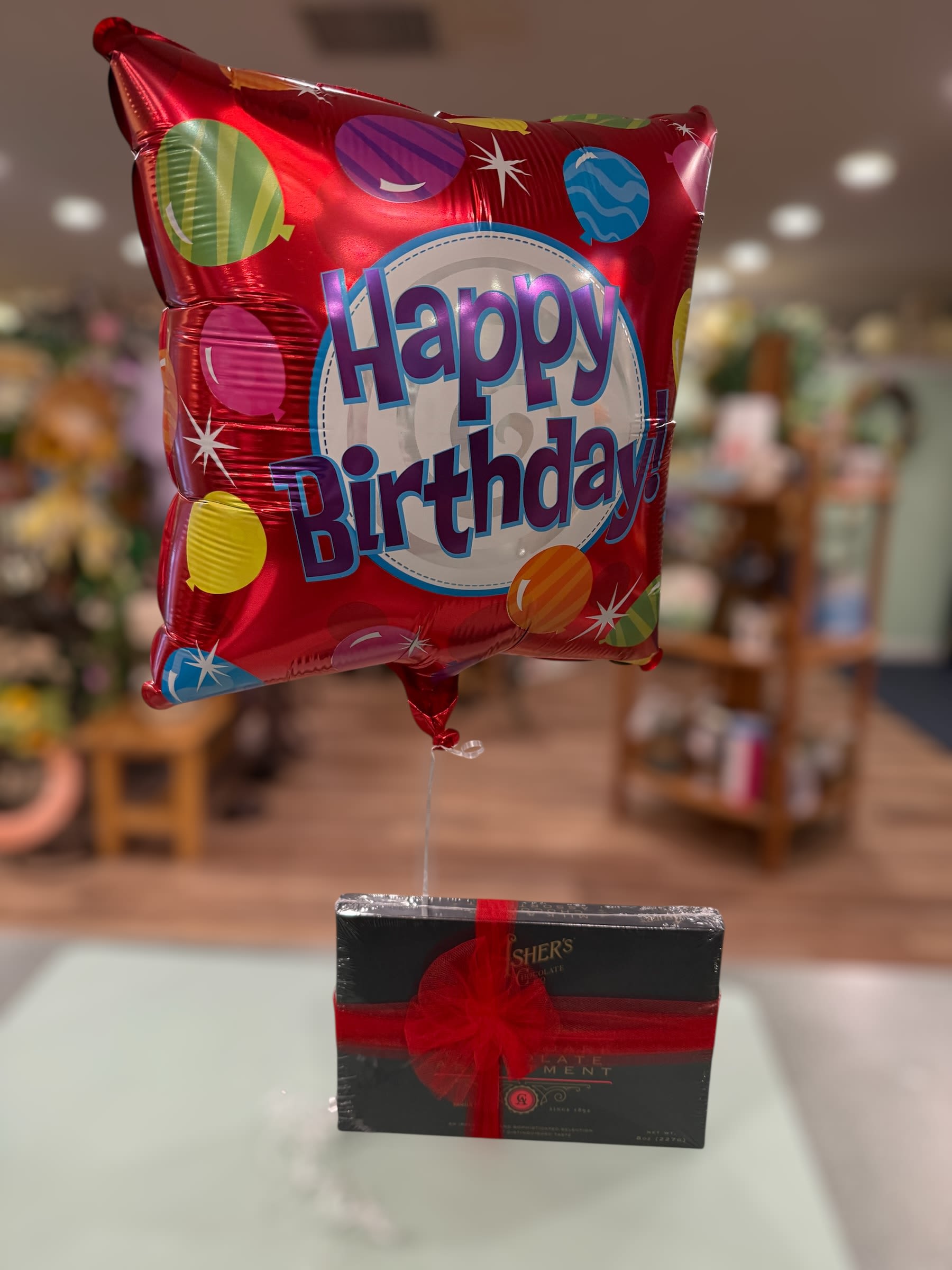 Birthday balloon with a box of chocolates tied below it