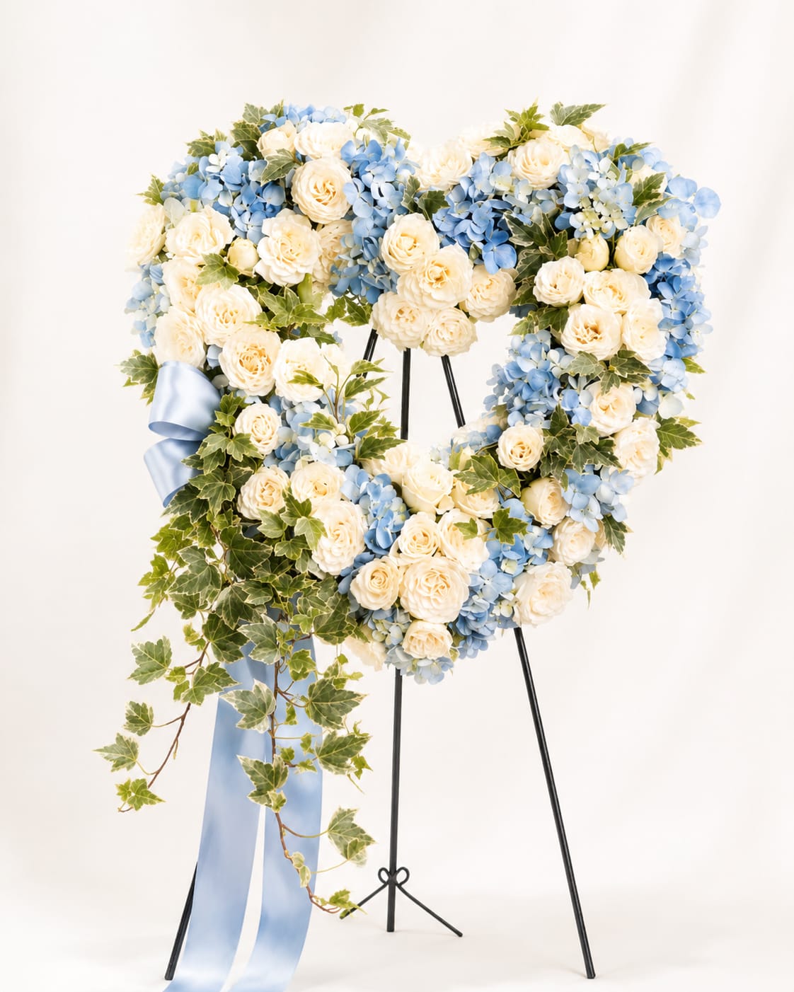Heart-shaped floral wreath with cream roses and blue hydrangeas on a stand