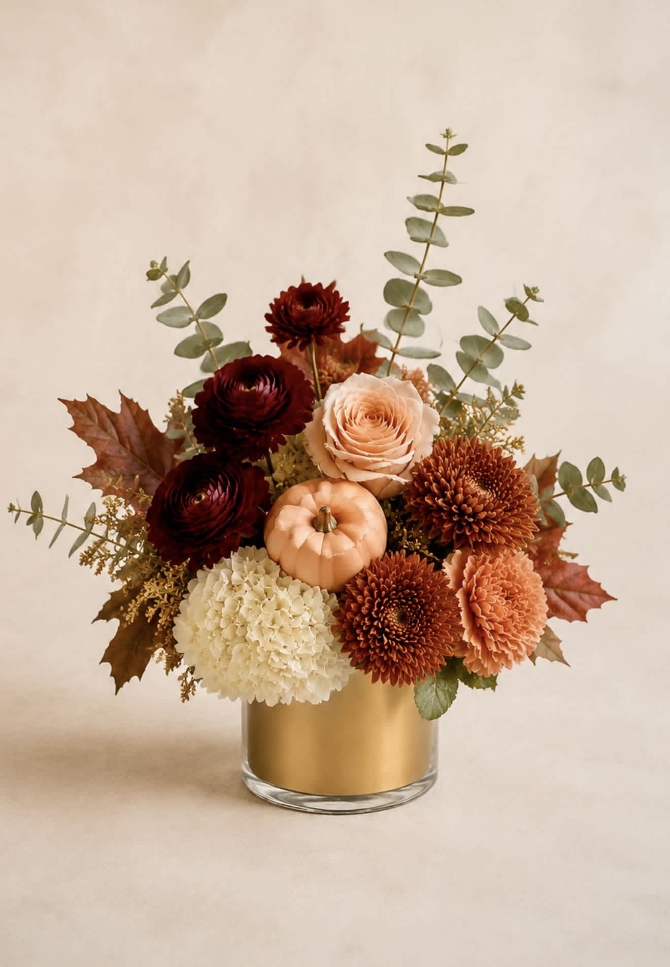 Autumn floral arrangement in a gold vase with a small pumpkin centerpiece