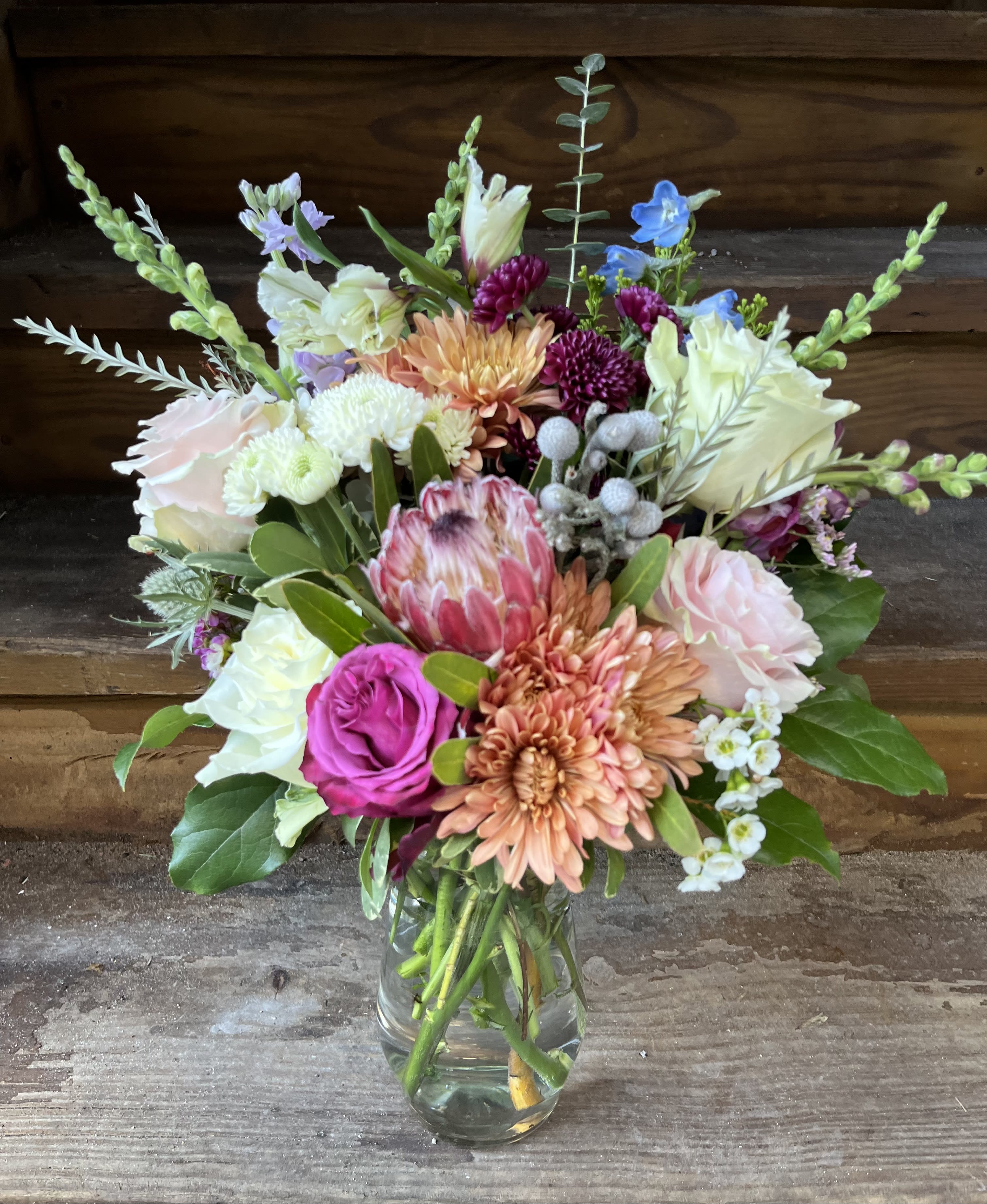 Mixed bouquet of pink, peach, white, and blue flowers in a glass vase