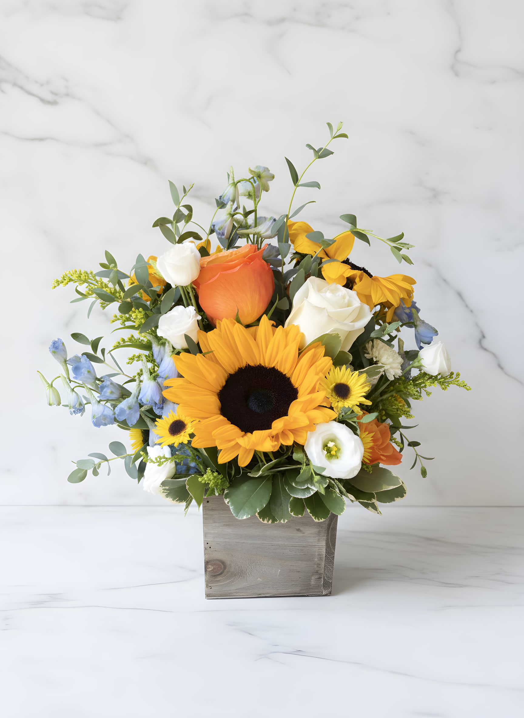 Sunflower bouquet with roses and blue flowers in a wooden box