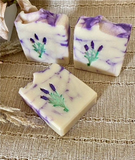 Three lavender and white decorative soap bars with pressed flowers