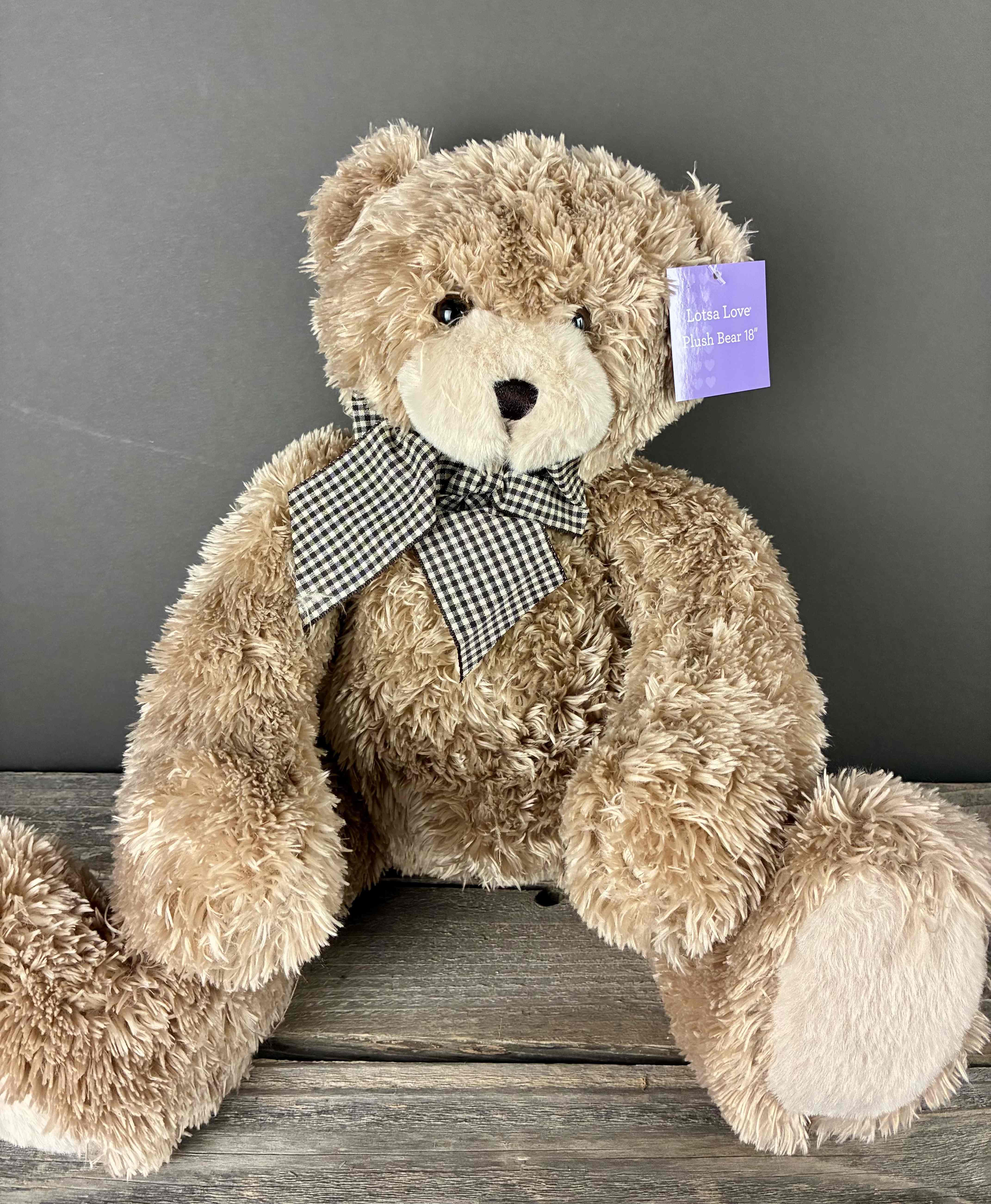 Large tan plush teddy bear with a checkered bow sitting on a wooden surface
