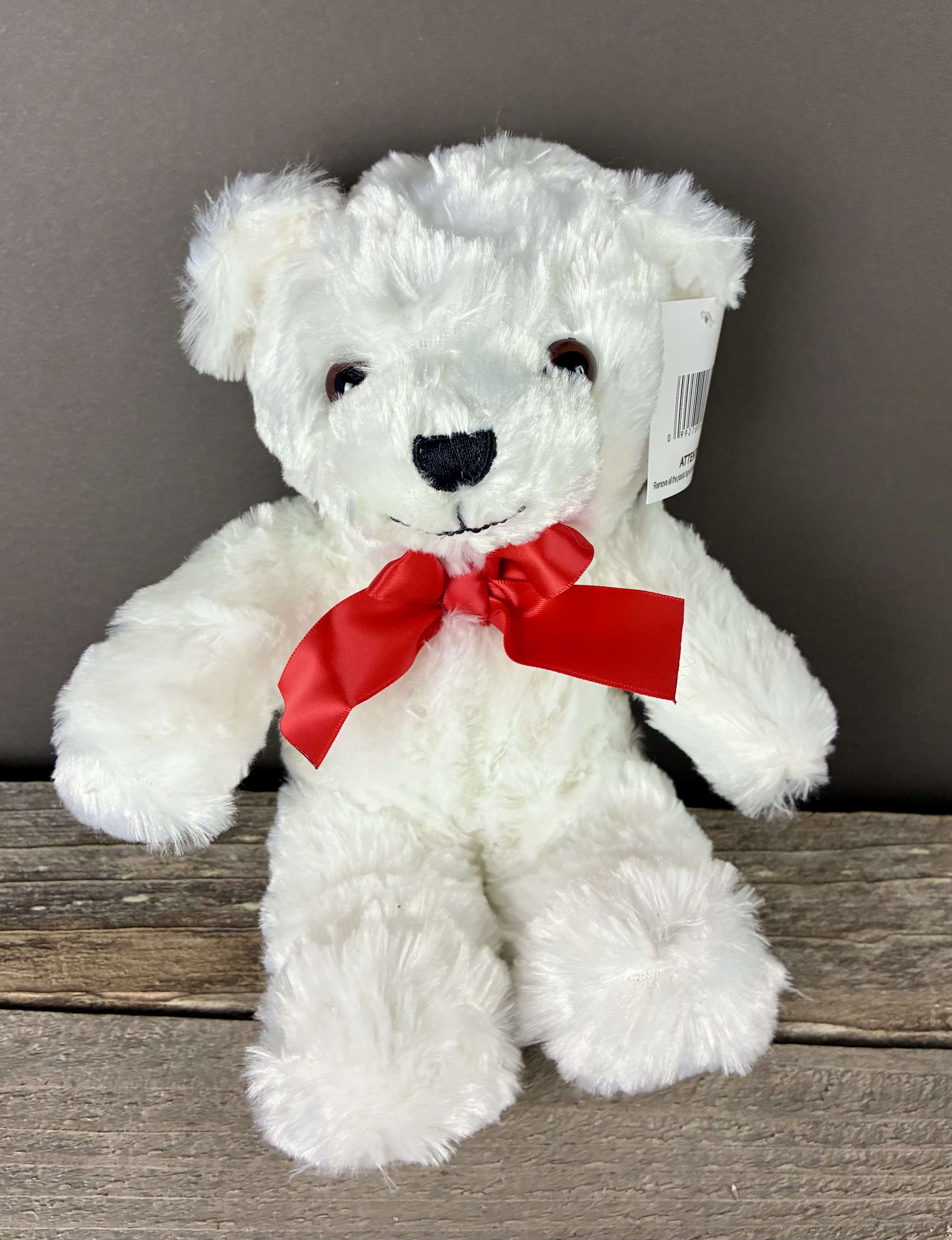White plush teddy bear with a red bow sitting on a wooden surface