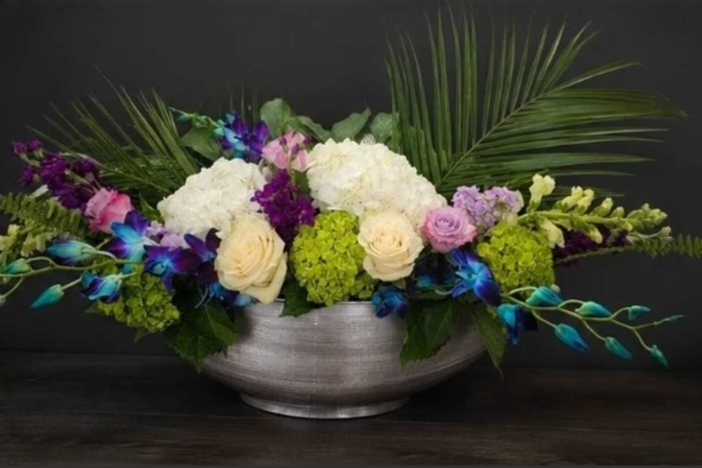 Majestic Voyage - Low, wide silver bowl filled with layered hydrangeas, roses, orchids and stock in white, pink, purple.
