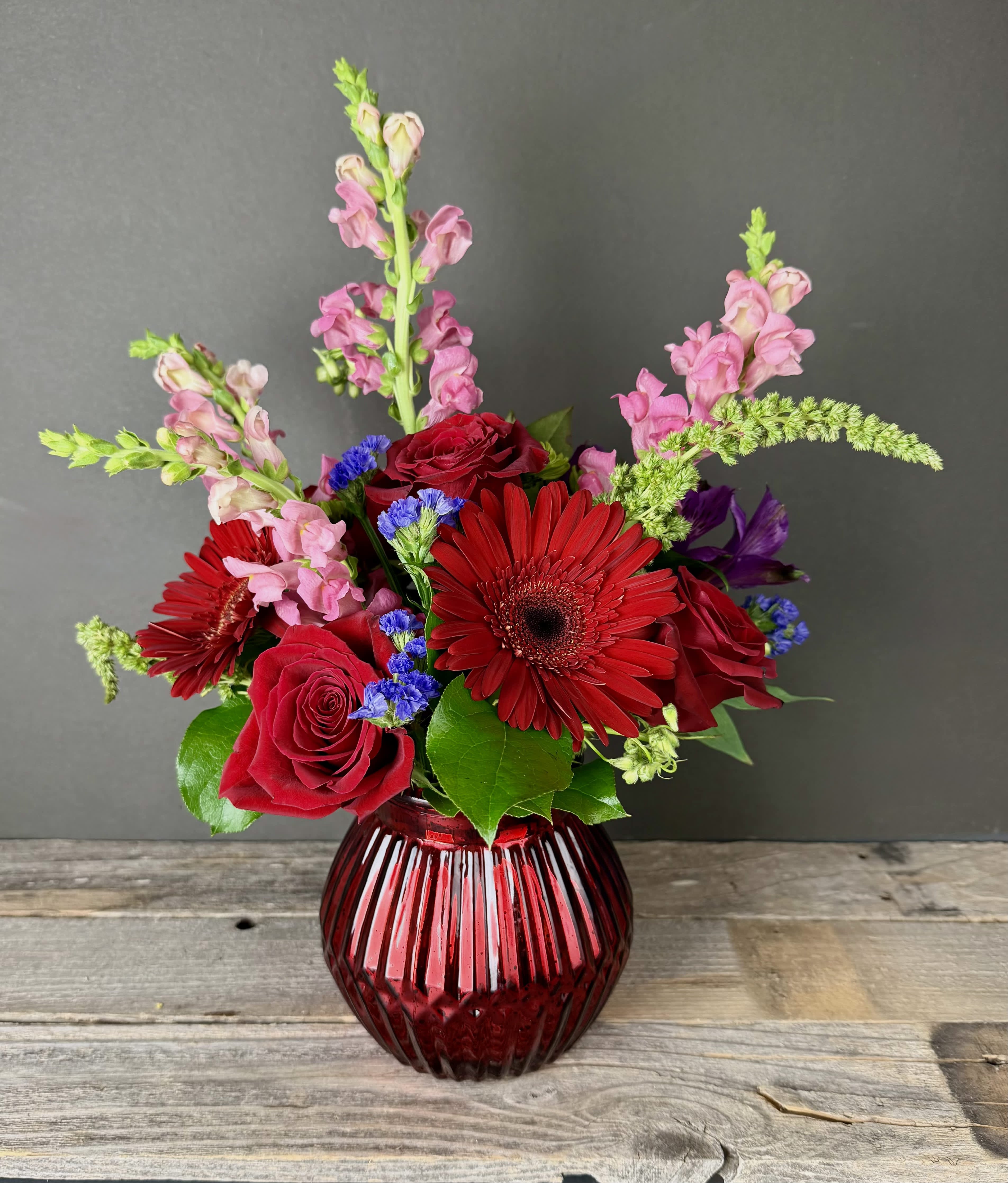 Red roses and gerbera daisies in a ribbed red glass vase
