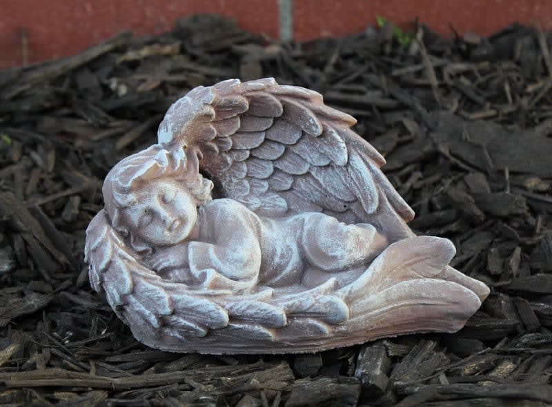 Small sleeping angel figurine with wings, resting on dark mulch