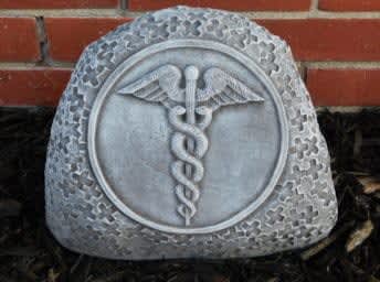 Gray memorial stone with a caduceus emblem in front of a brick wall