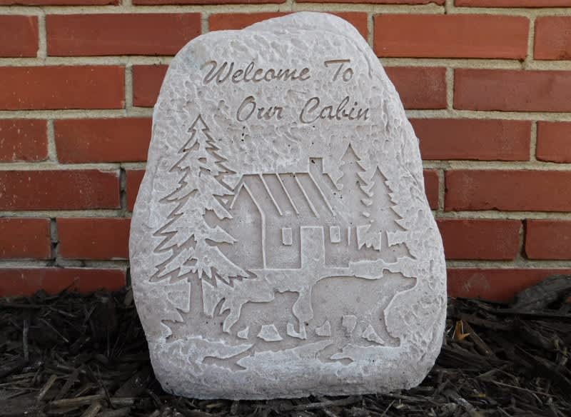 Carved stone plaque with a cabin, trees, and bears against a brick wall