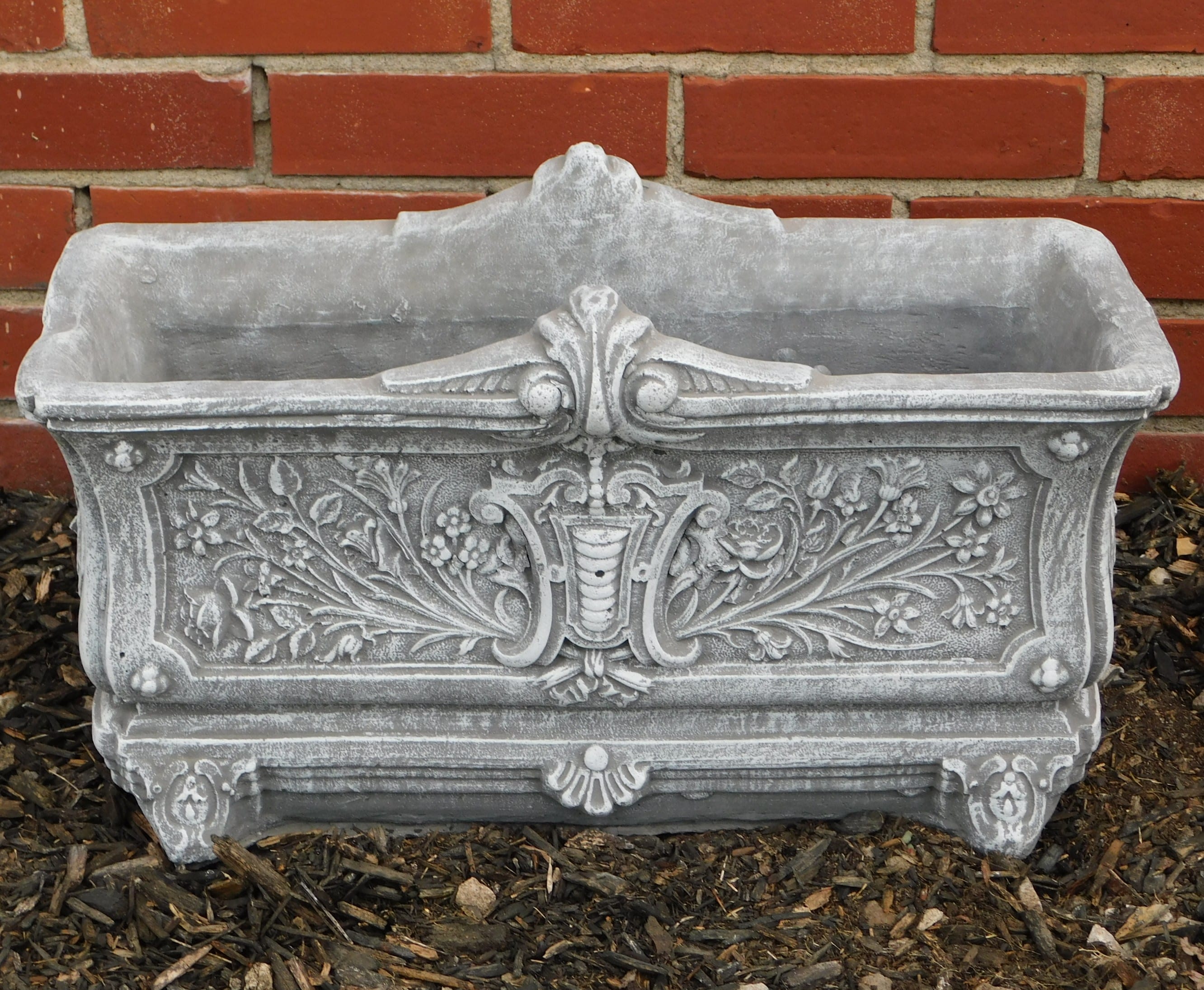 Ornate gray stone planter box against a brick wall