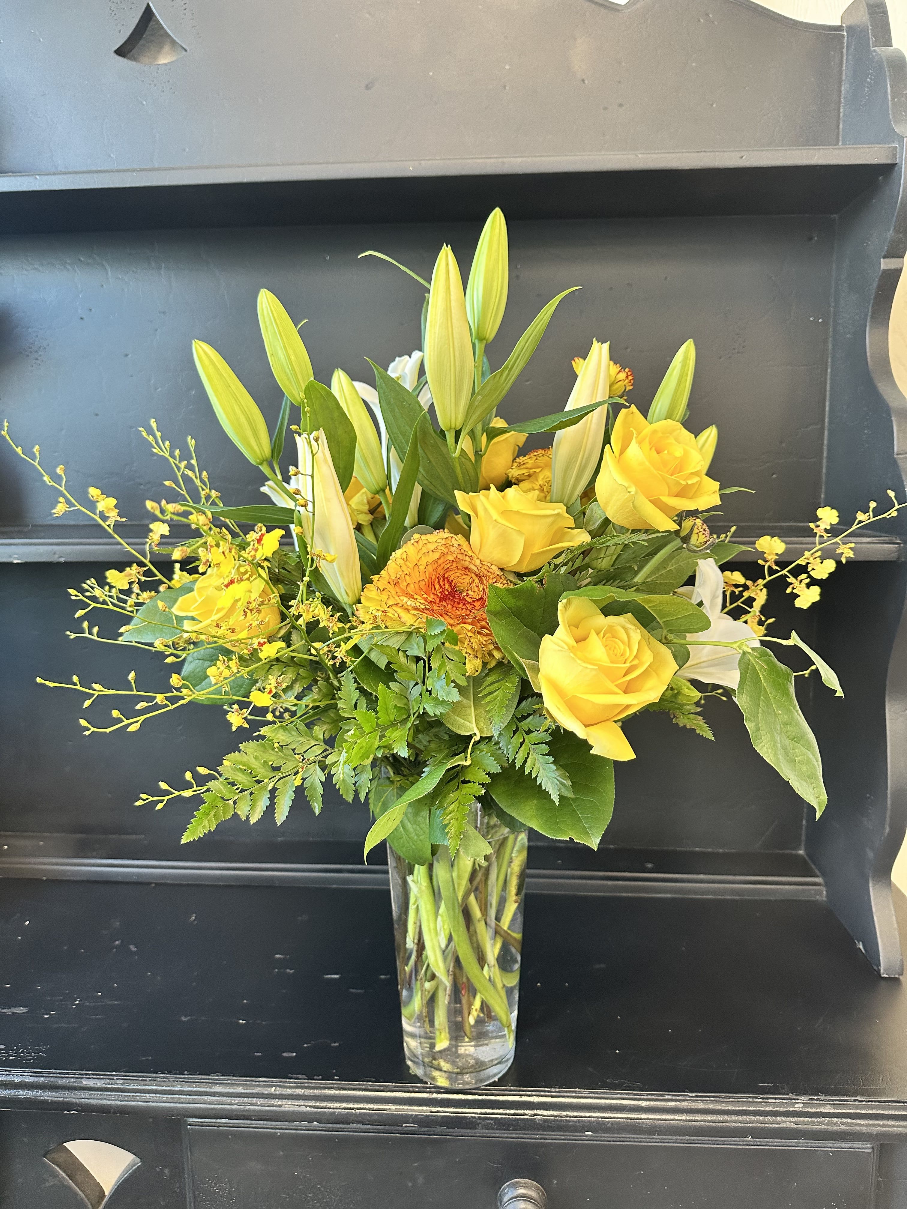 Yellow roses and lilies arranged in a clear glass vase