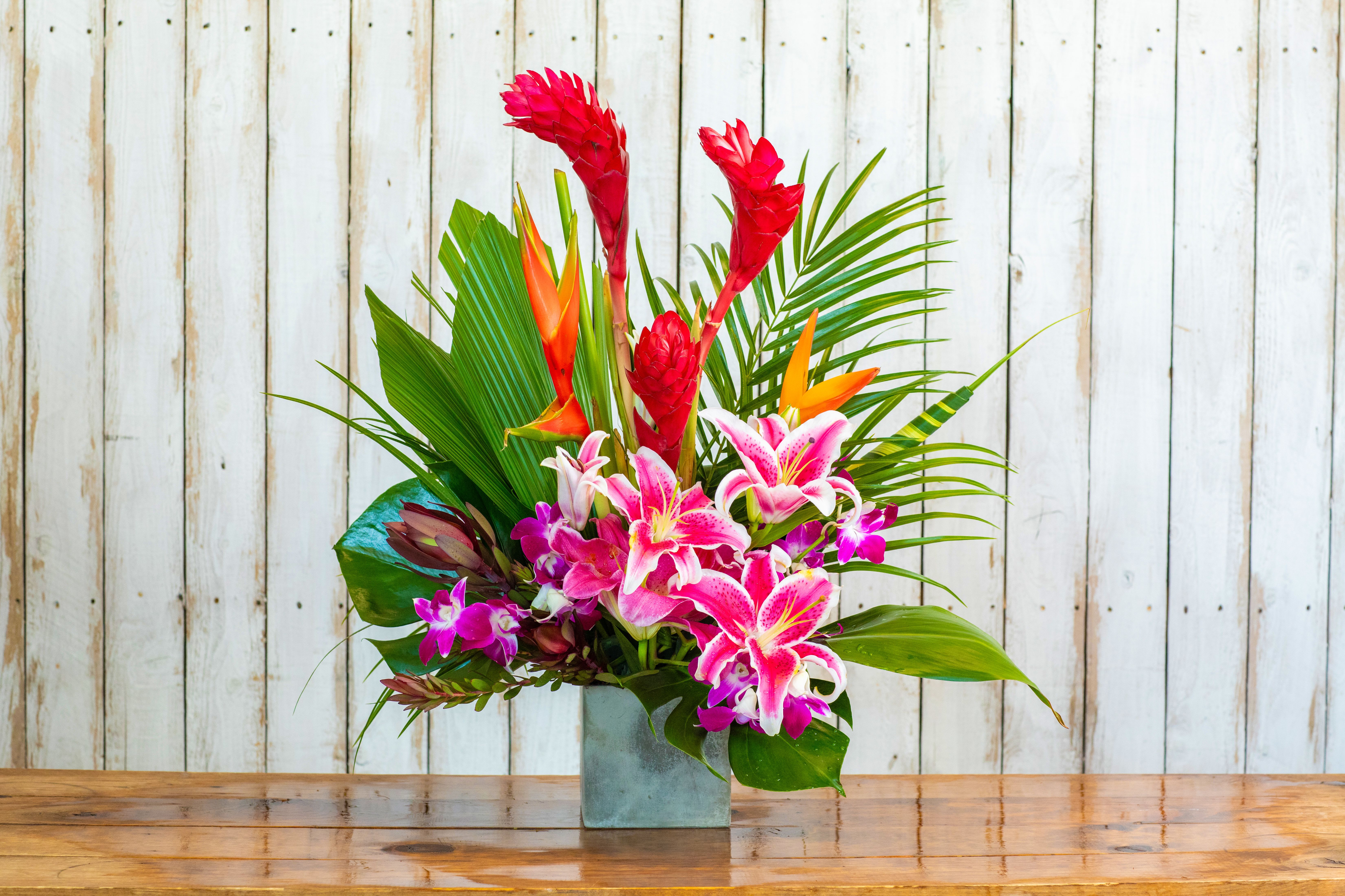Tropical flower arrangement with pink lilies and red ginger in a square vase