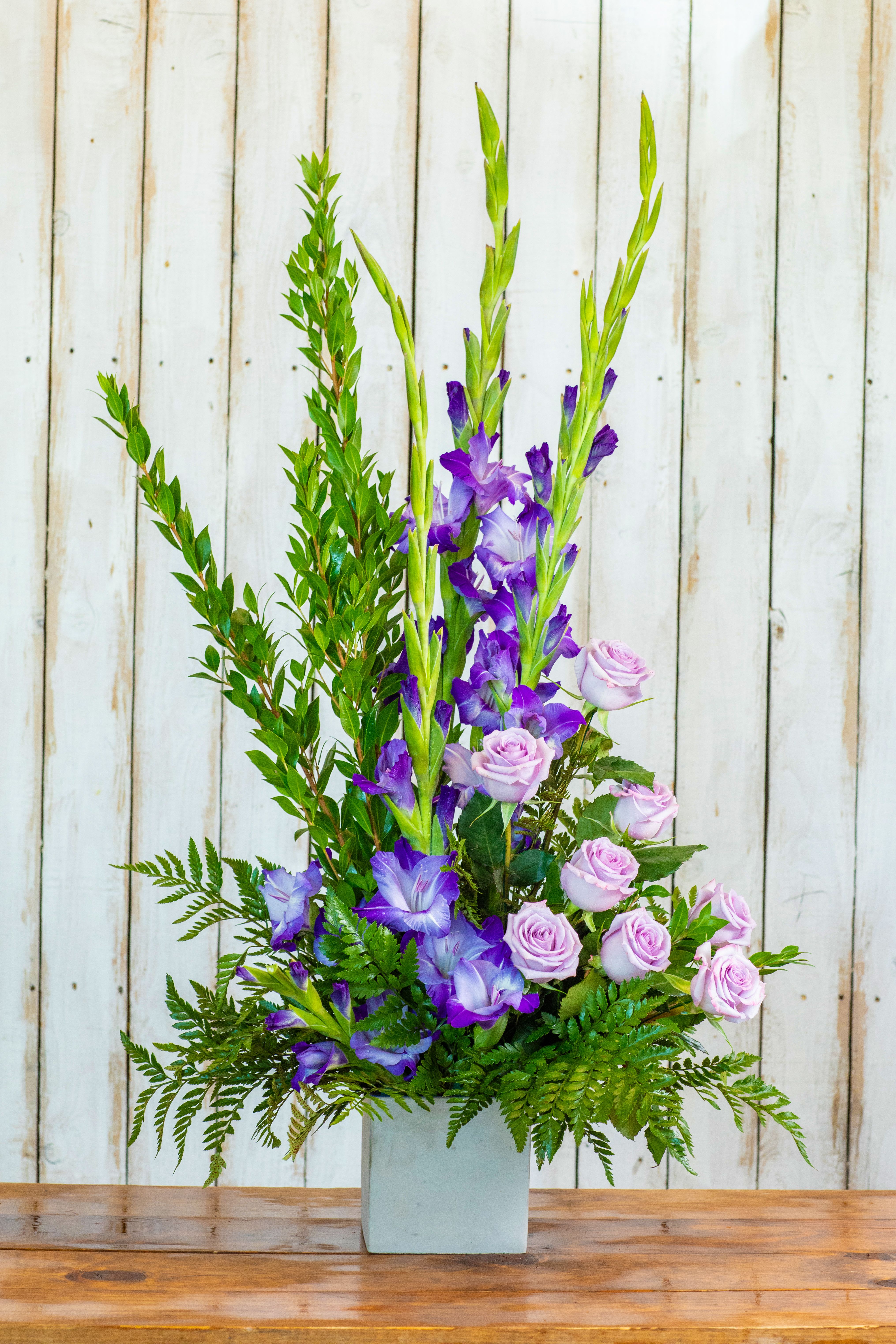 Tall floral arrangement with purple flowers and pale pink roses in a square vase