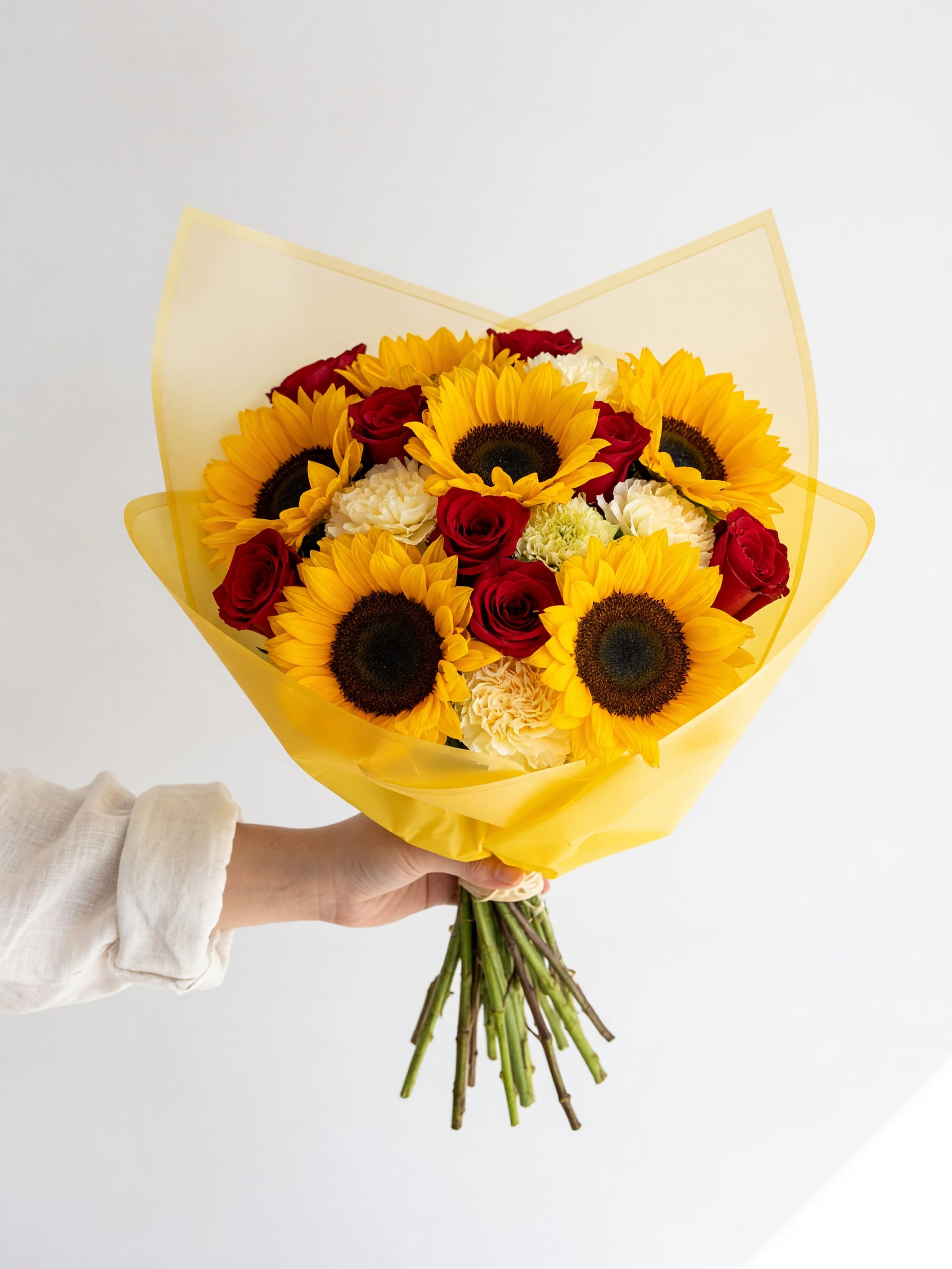 Golden Sunshine™ Hand-Tied Bouquet - Radiate happiness with our Golden Sunshine™ Hand-Tied Bouquet, a stunning combination of radiant sunflowers, classic red roses, and soft white carnations wrapped in elegant waterproof yellow floral paper.  This handcrafted bouquet captures the warmth of sunshine and the beauty of fresh blooms, making it the perfect gift to celebrate life’s special moments. Whether you’re sending birthday wishes, congratulations, love, appreciation, or simply brightening someone’s day, this bouquet is guaranteed to make a lasting impression.  Designed with premium fresh flowers by the expert floral designers at Tommy Austin Florist, each bouquet is carefully arranged and hand-wrapped for a modern, stylish presentation.  Flowers Included  * Premium Sunflowers * Red Roses * White Carnations * chrysanthemum  * Fresh Seasonal Greenery * Elegant Waterproof Floral  Wrap