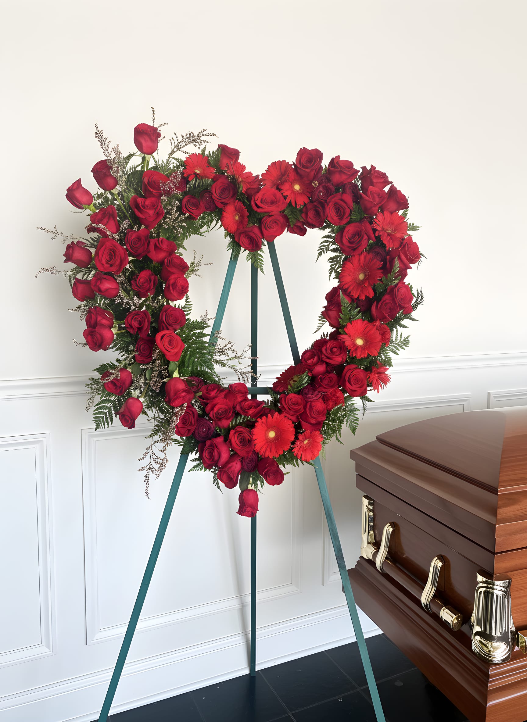 Forever in My Heart™ Standing Heart - Honor a life filled with love through our Forever in My Heart™ Standing Heart Tribute. This breathtaking open-heart standing spray is handcrafted with luxurious red roses, vibrant red gerbera daisies, elegant accent flowers, and lush premium greenery to create a heartfelt expression of everlasting love and remembrance.  Displayed on a standing easel, this elegant tribute is designed to surround the family with warmth, compassion, and comfort while celebrating a beautiful life. The open-heart design symbolizes a love that never ends, making it a meaningful choice for funeral services, memorials, and celebrations of life.  Each tribute is thoughtfully designed by the compassionate floral artisans at Tommy Austin Florist, using only the freshest premium flowers. Every sympathy tribute is handcrafted with the freshest flowers available. If substitutions are necessary due to seasonal availability, we will preserve the same elegant style, rich color palette, and premium value. 