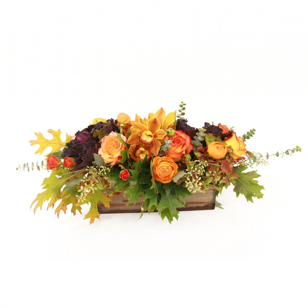 lovely centerpiece -   long low wooden vase arrangement featuring flowering kale, circus roses, rannunculus, spray roses and greens  