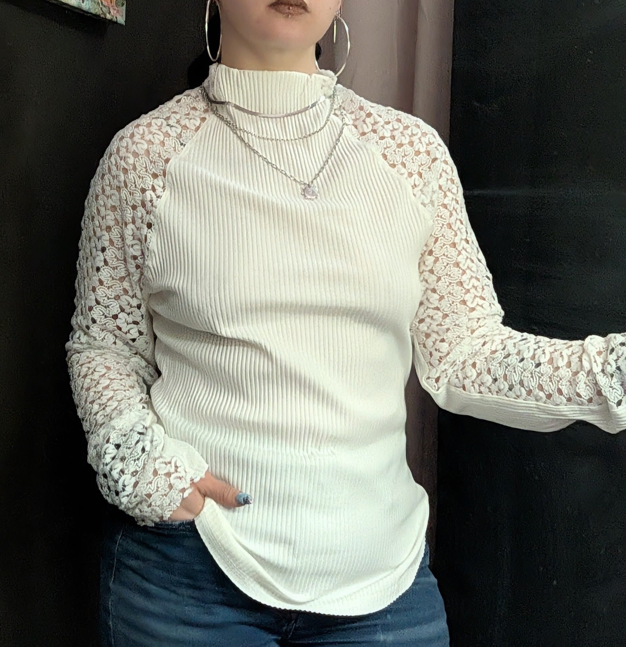 Woman wearing a cream ribbed top with lace sleeves and jeans