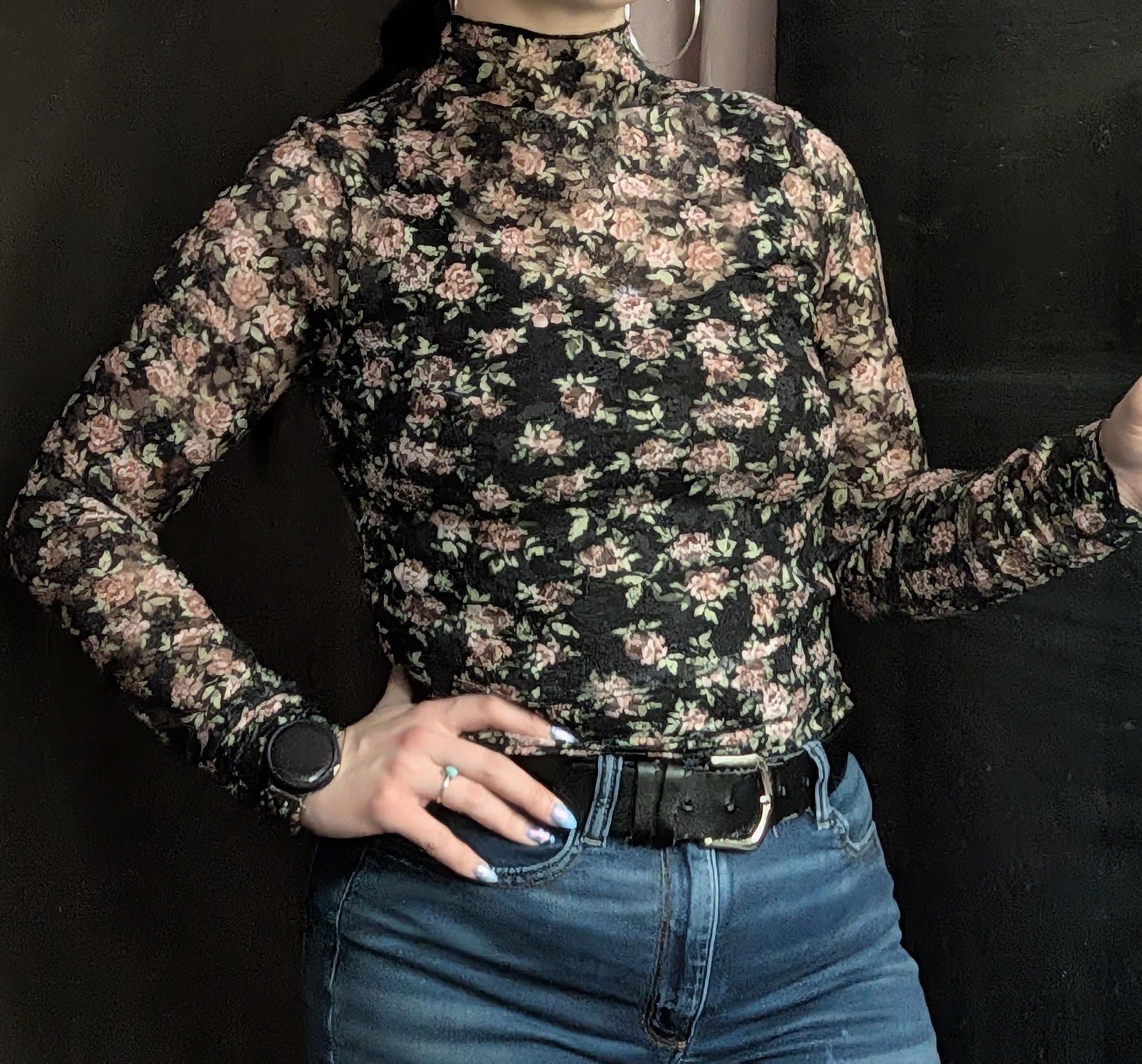 Person wearing a black floral long-sleeve top and blue jeans