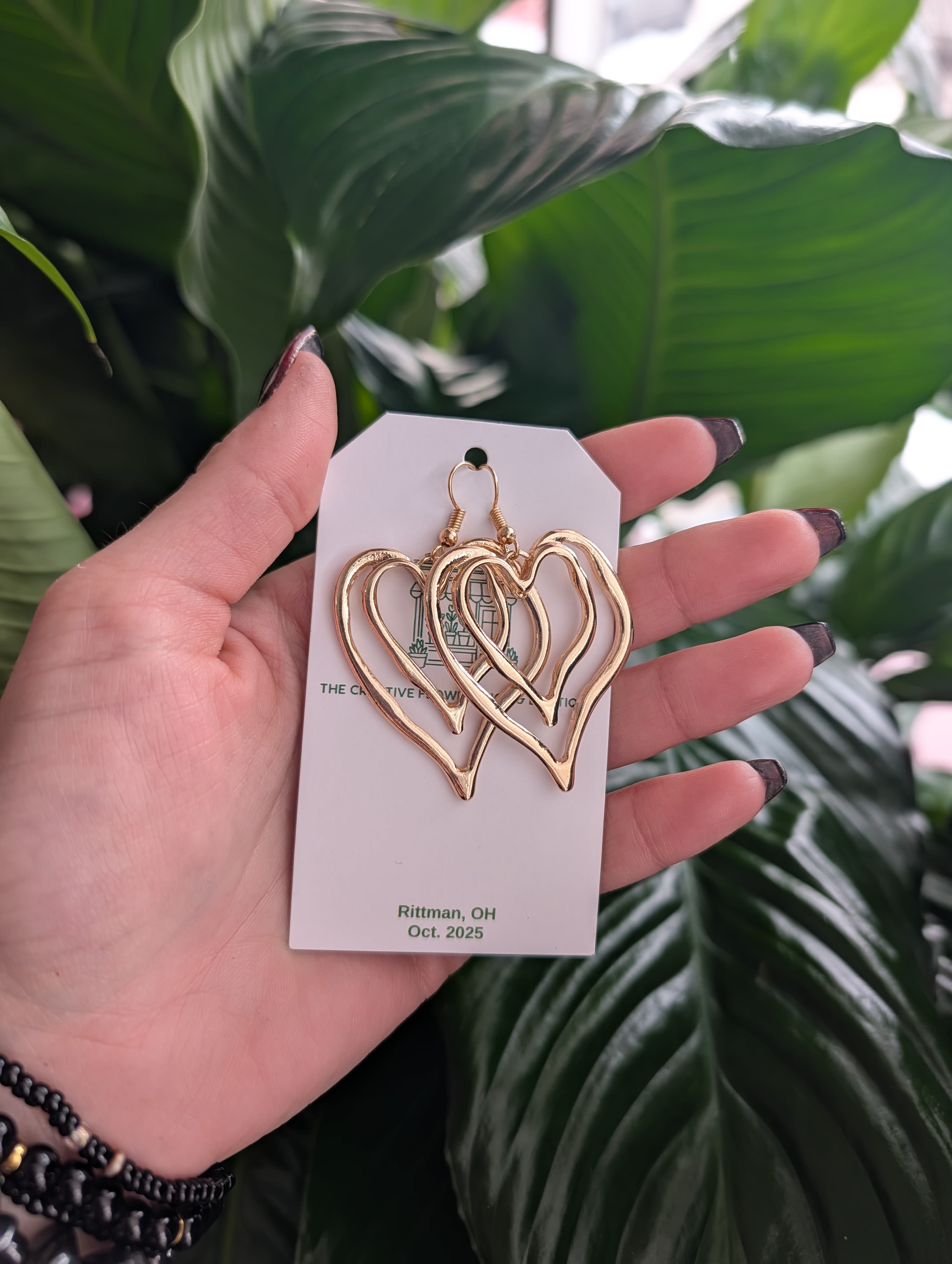 Gold heart-shaped earrings on a display card held in a hand