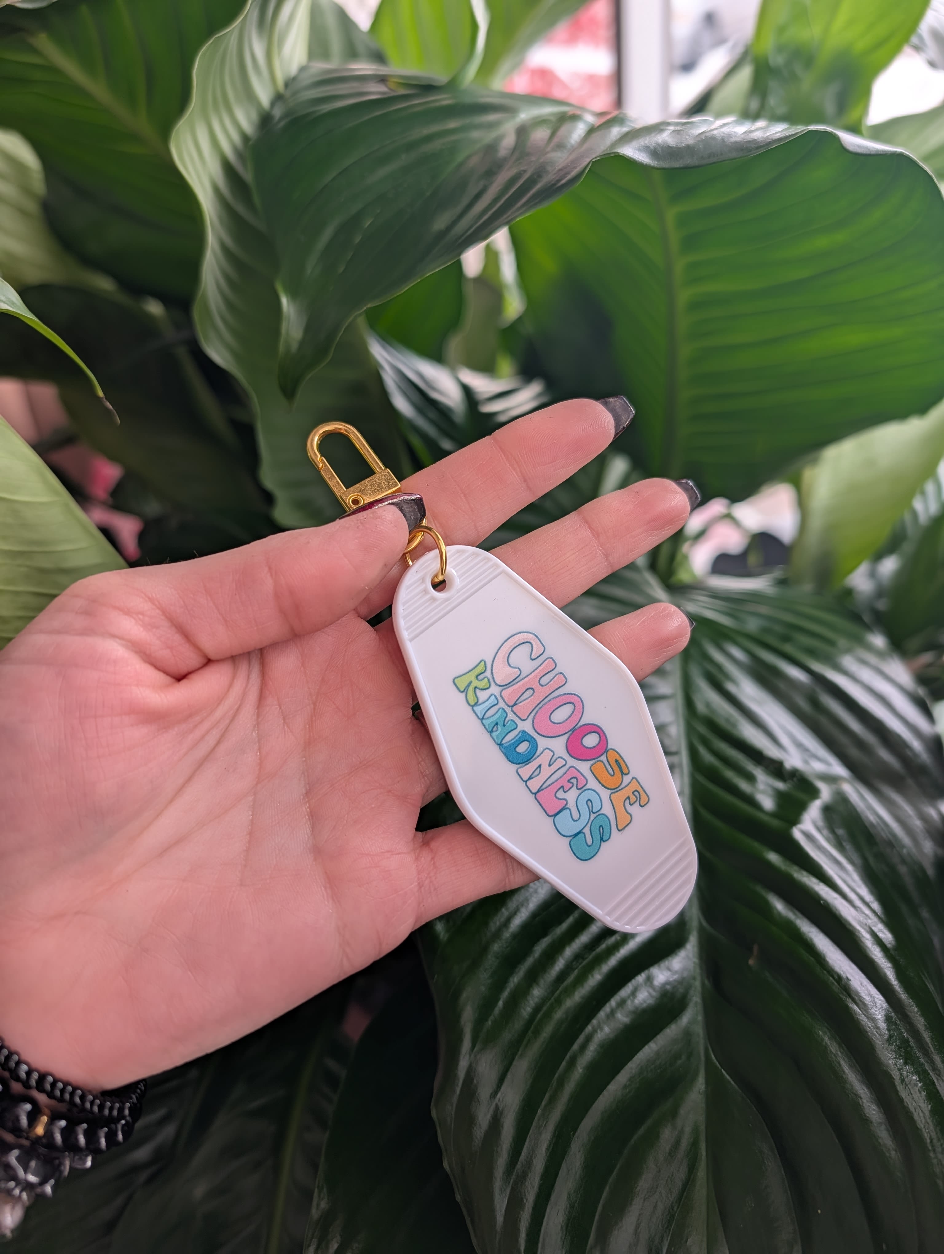 Hand holding a keychain tag in front of large green leaves