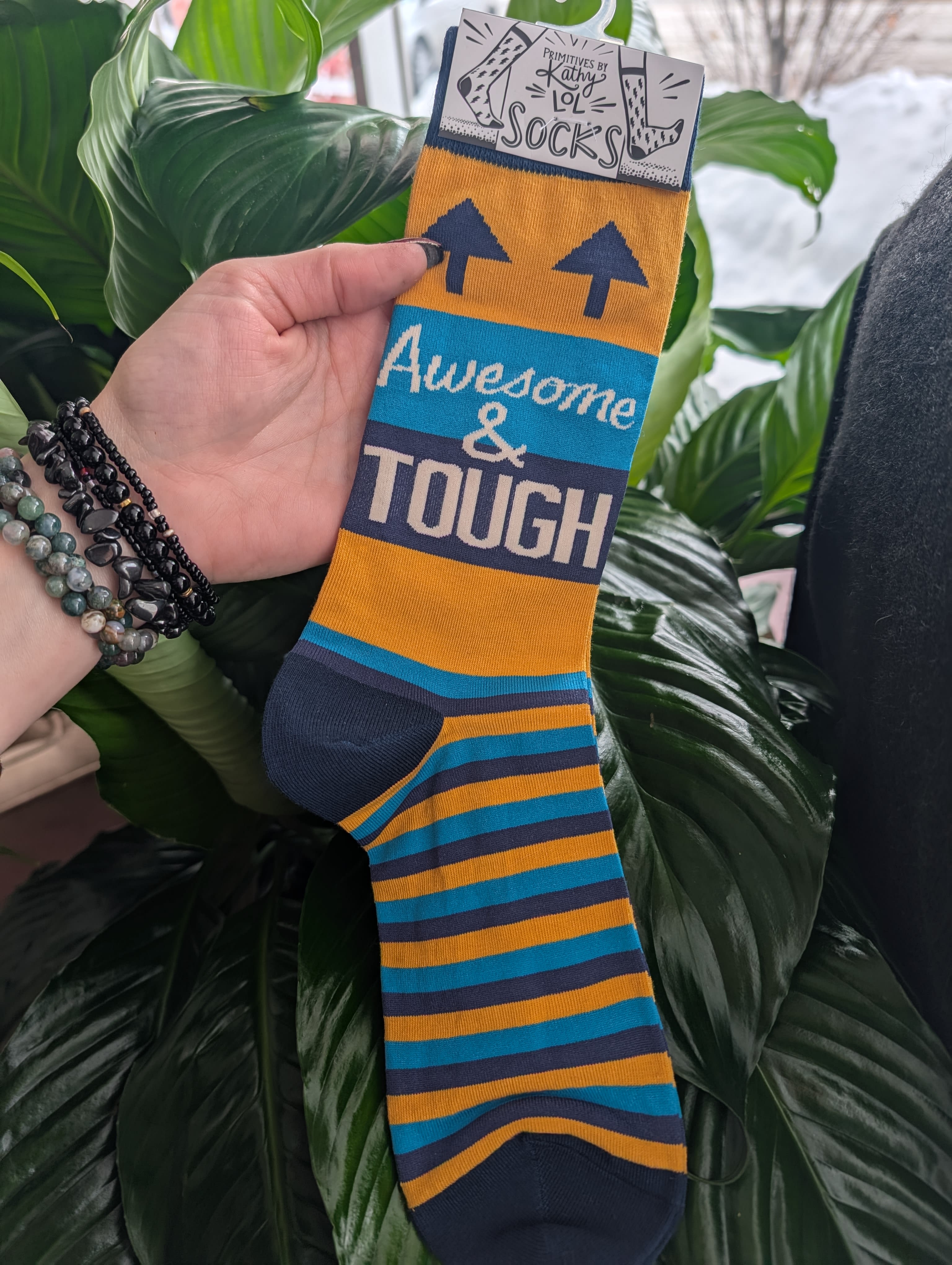 Hand holding a pair of striped novelty socks with "Awesome &amp; Tough" text