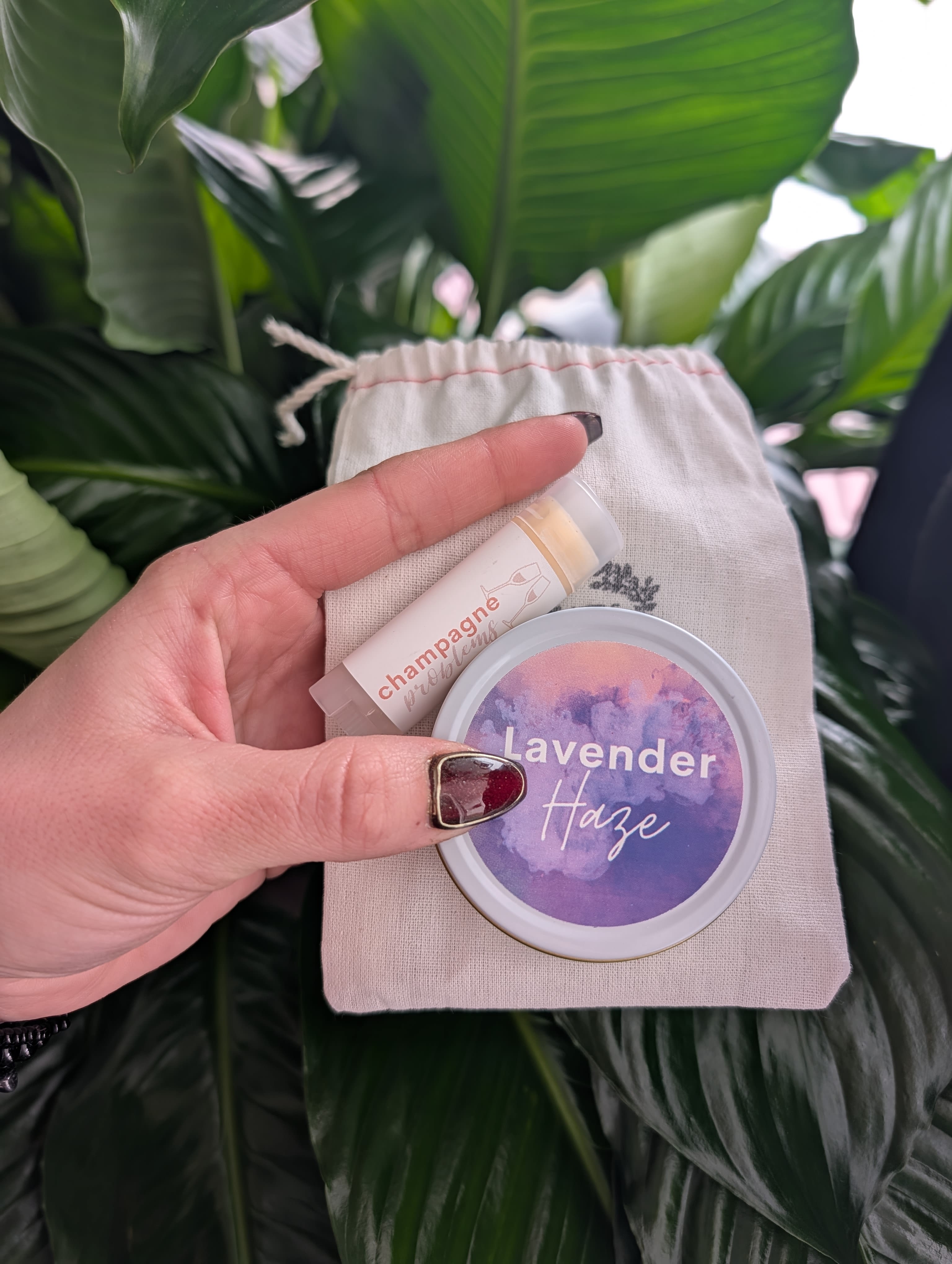 Hand holding a lavender haze lip balm and a champagne lip balm in a small pouch