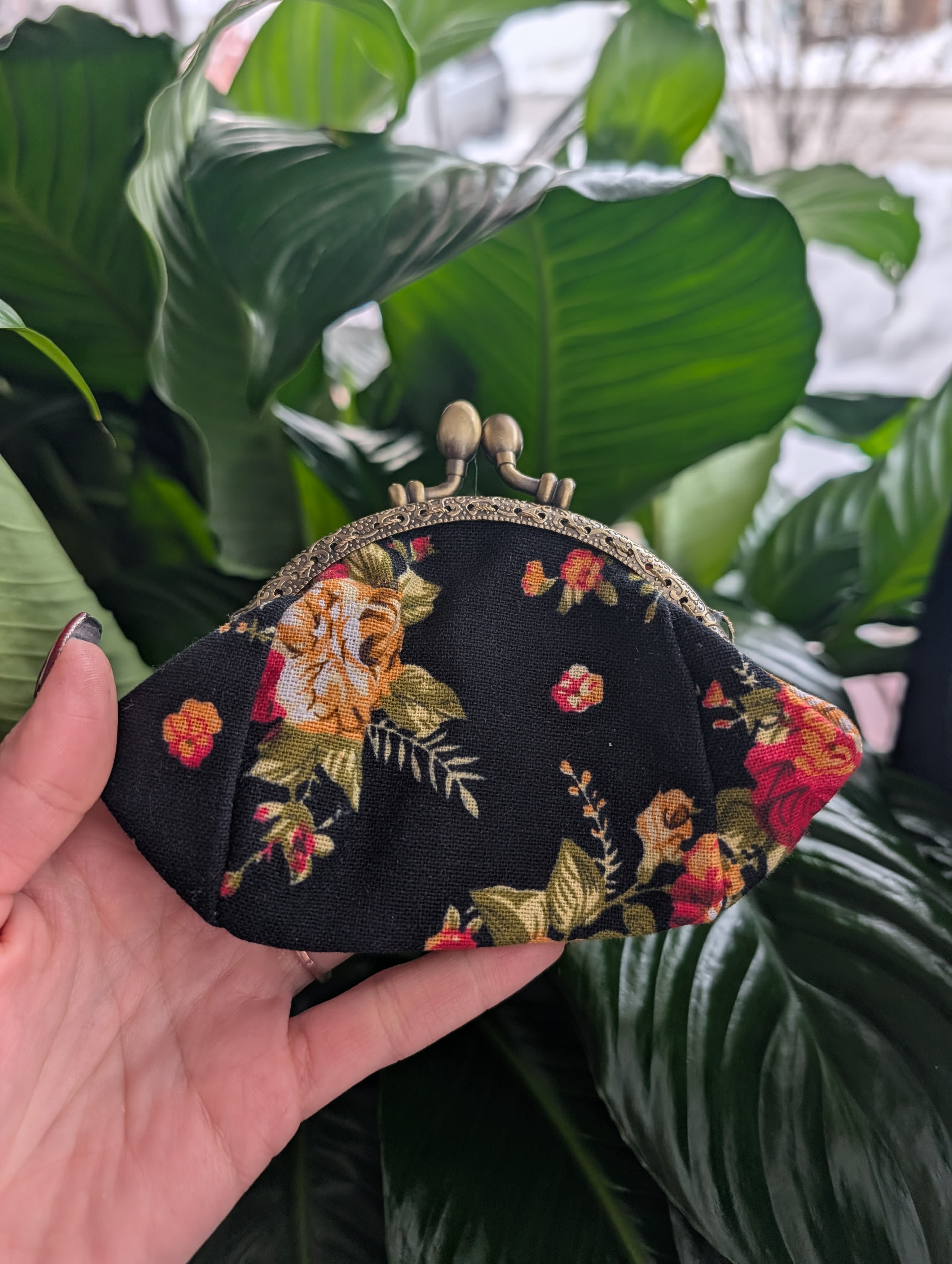 Floral-print fabric coin purse with a metal clasp held in a hand