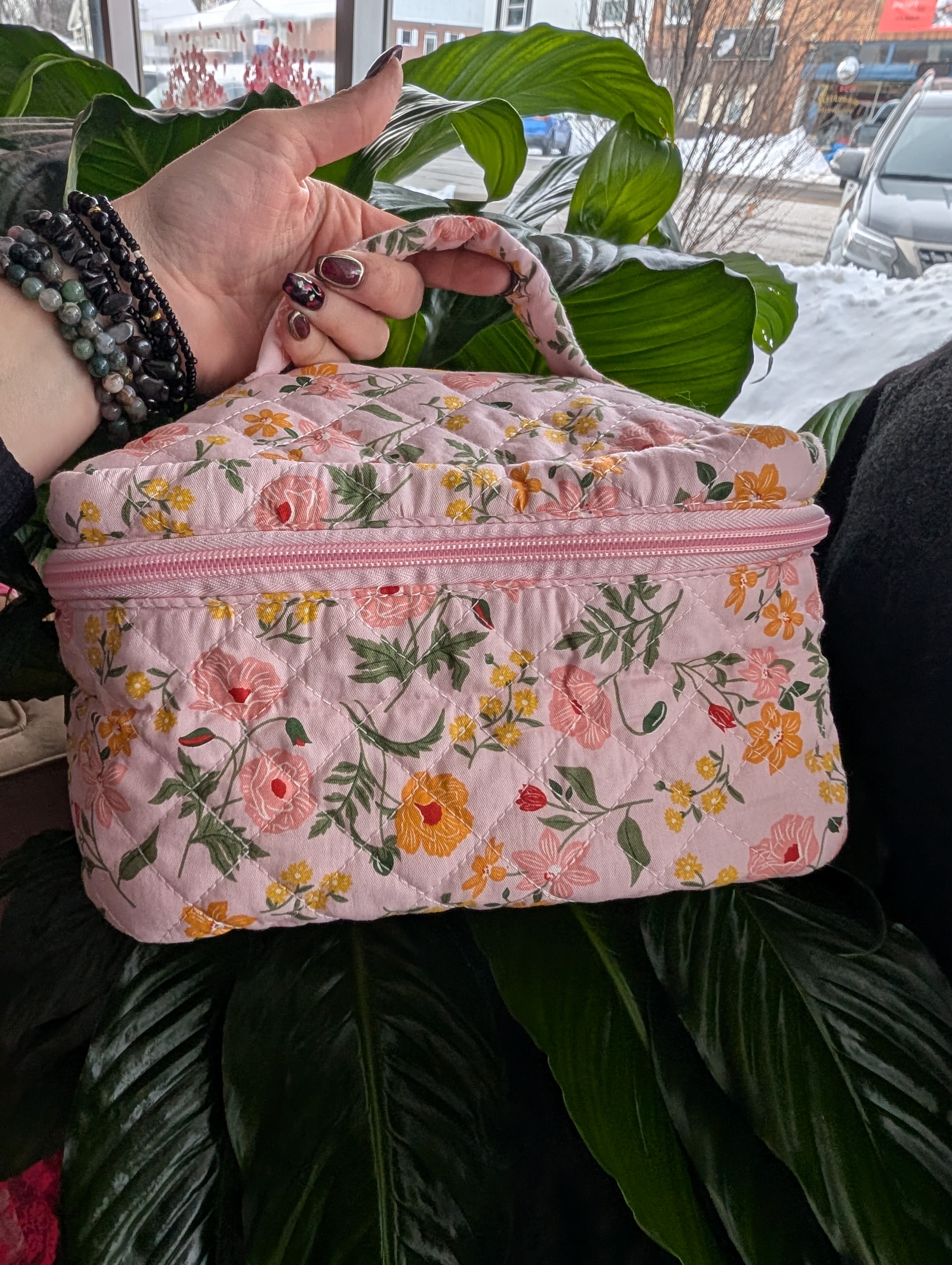 Pink floral quilted zippered bag held in front of a large green plant