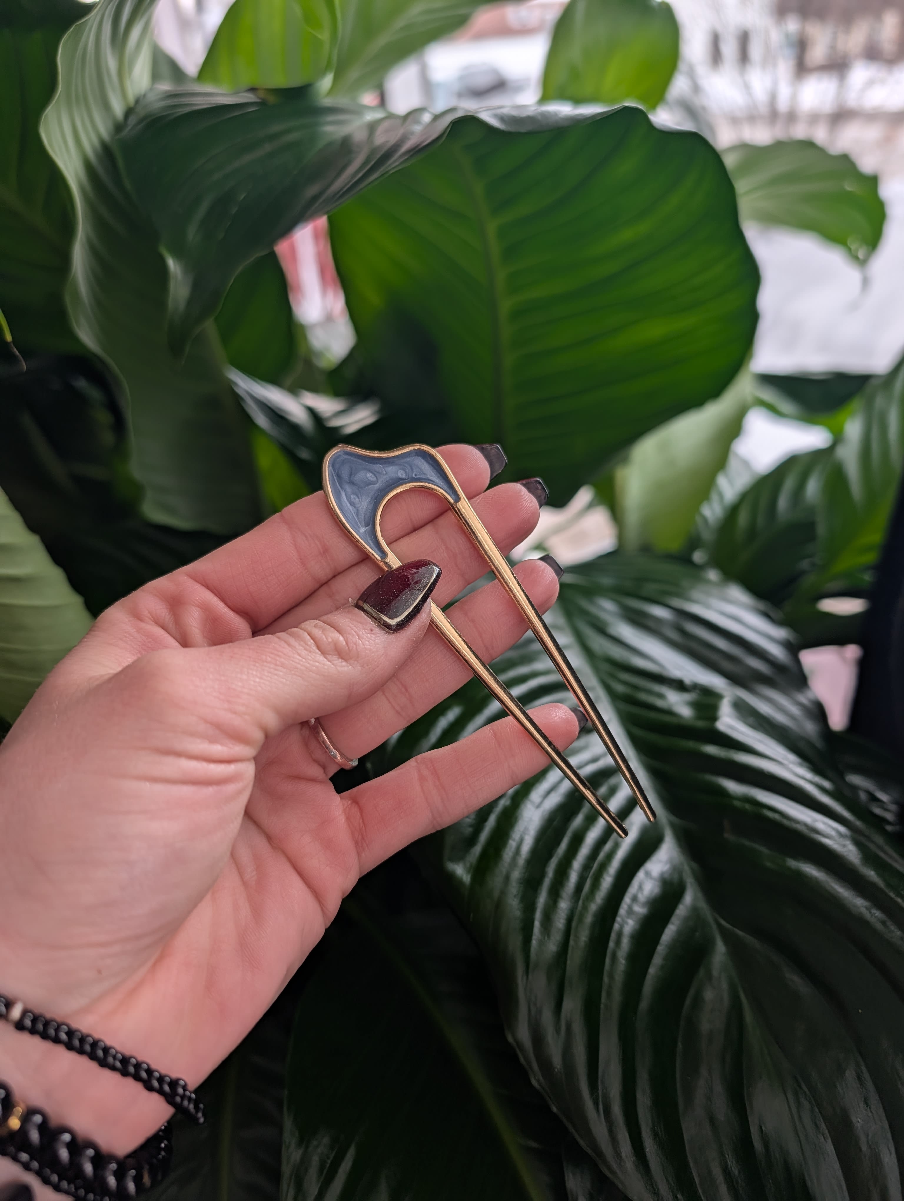 Hand holding a gold floral pick in front of large green leaves