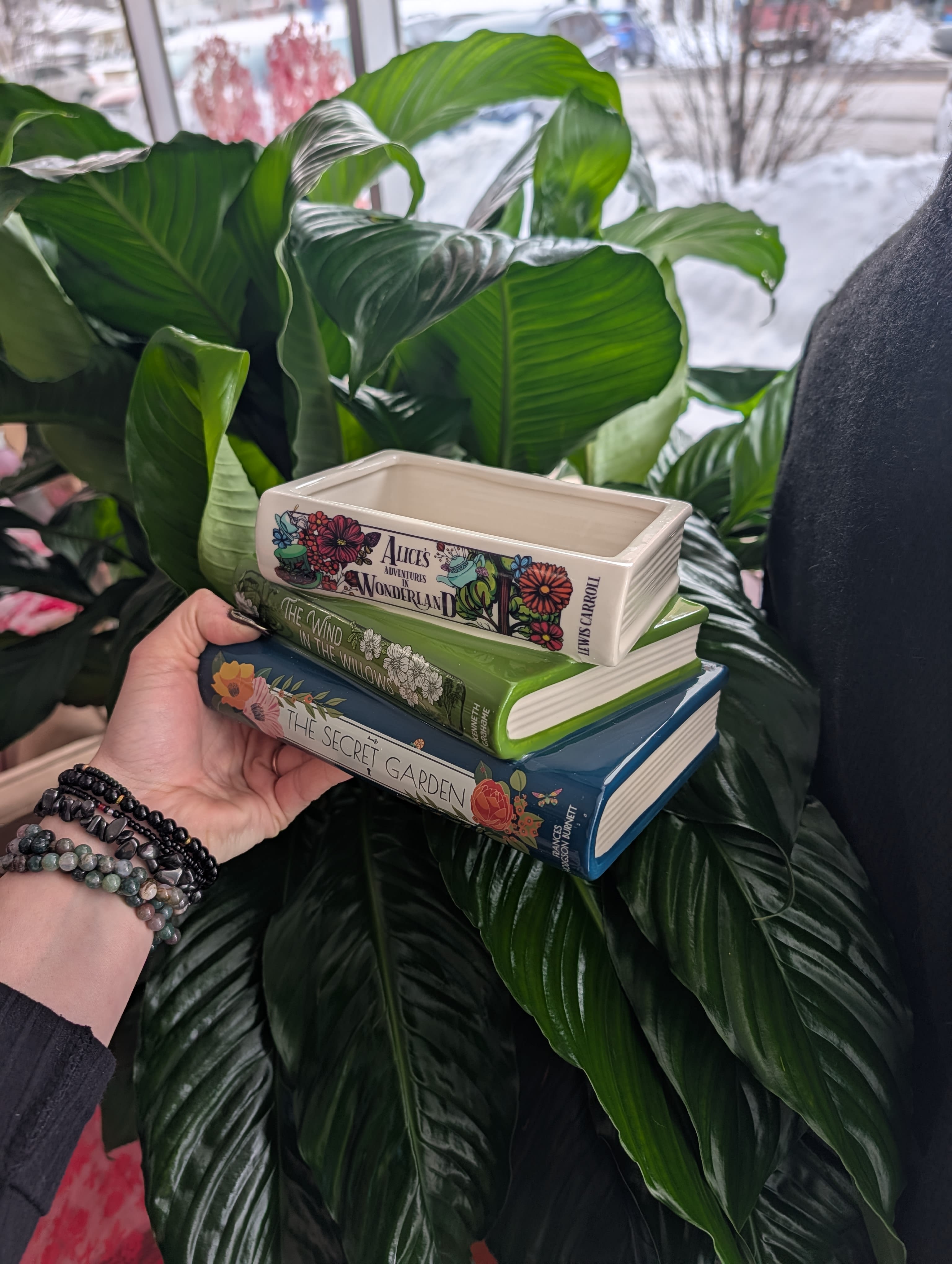 Stack of three decorative book-shaped planters held in front of large green leaves.