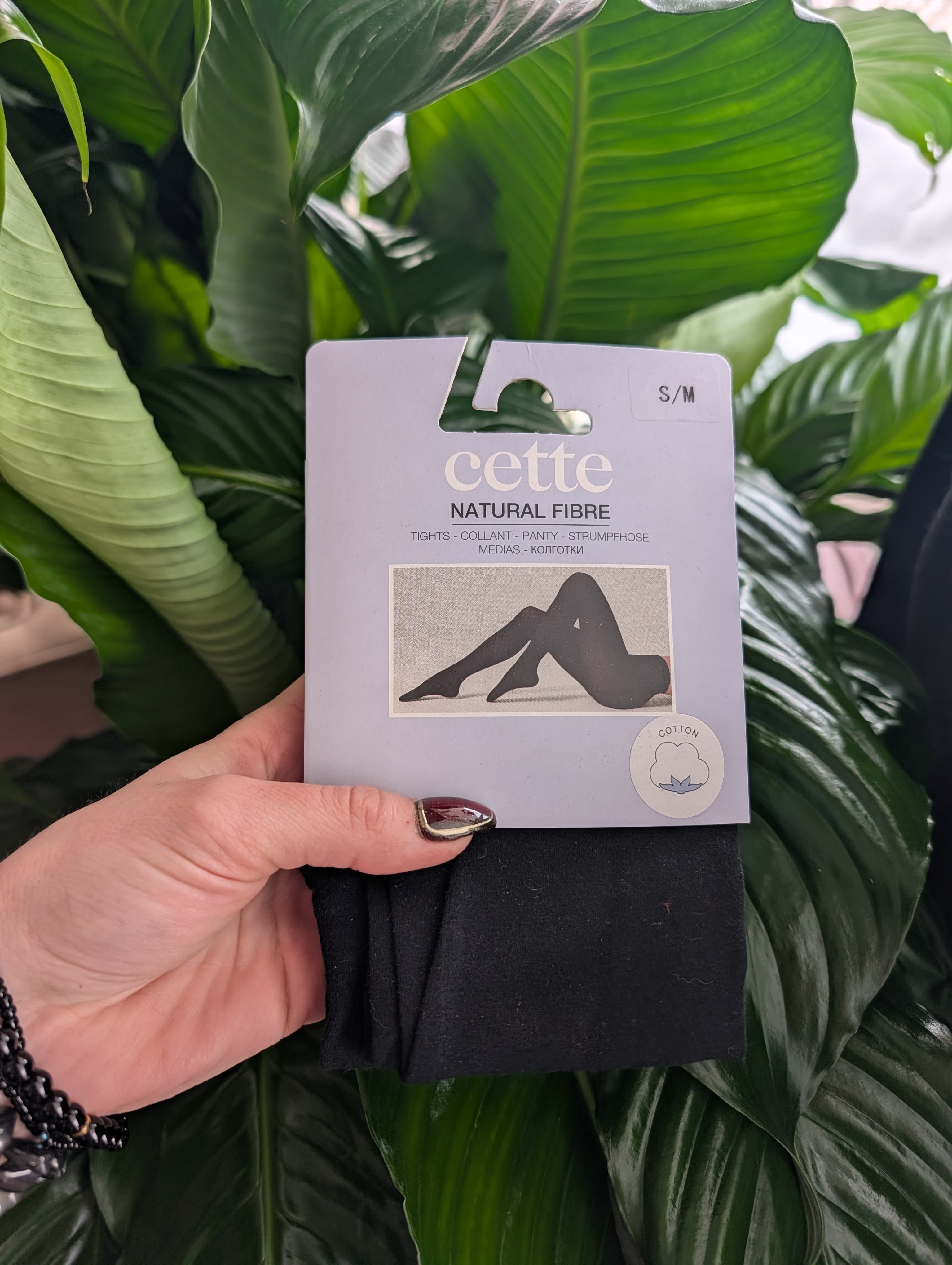 Hand holding packaged black tights in front of large green leaves