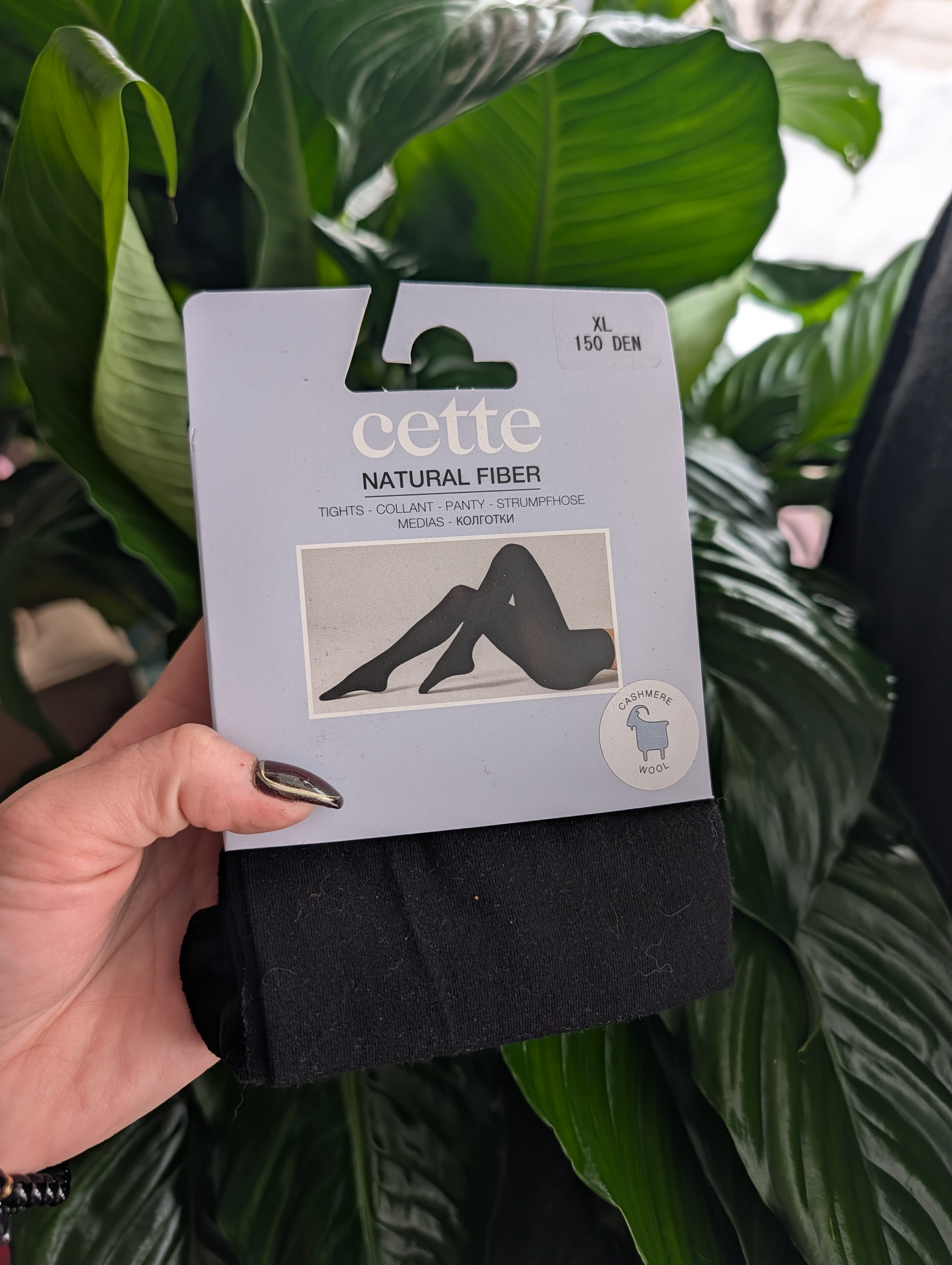Hand holding packaged black tights in front of green leaves