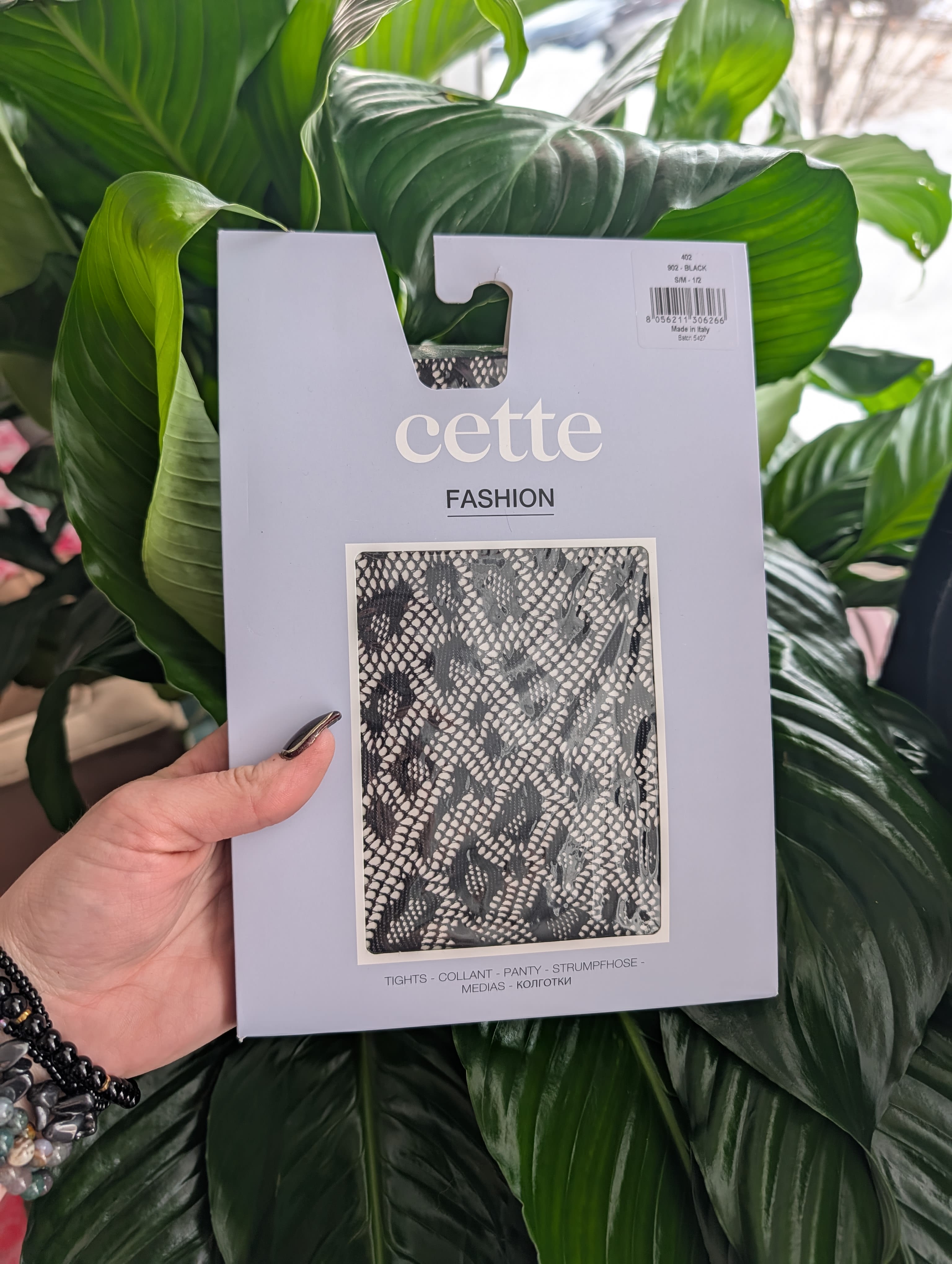 Packaged black patterned tights held in front of large green leaves
