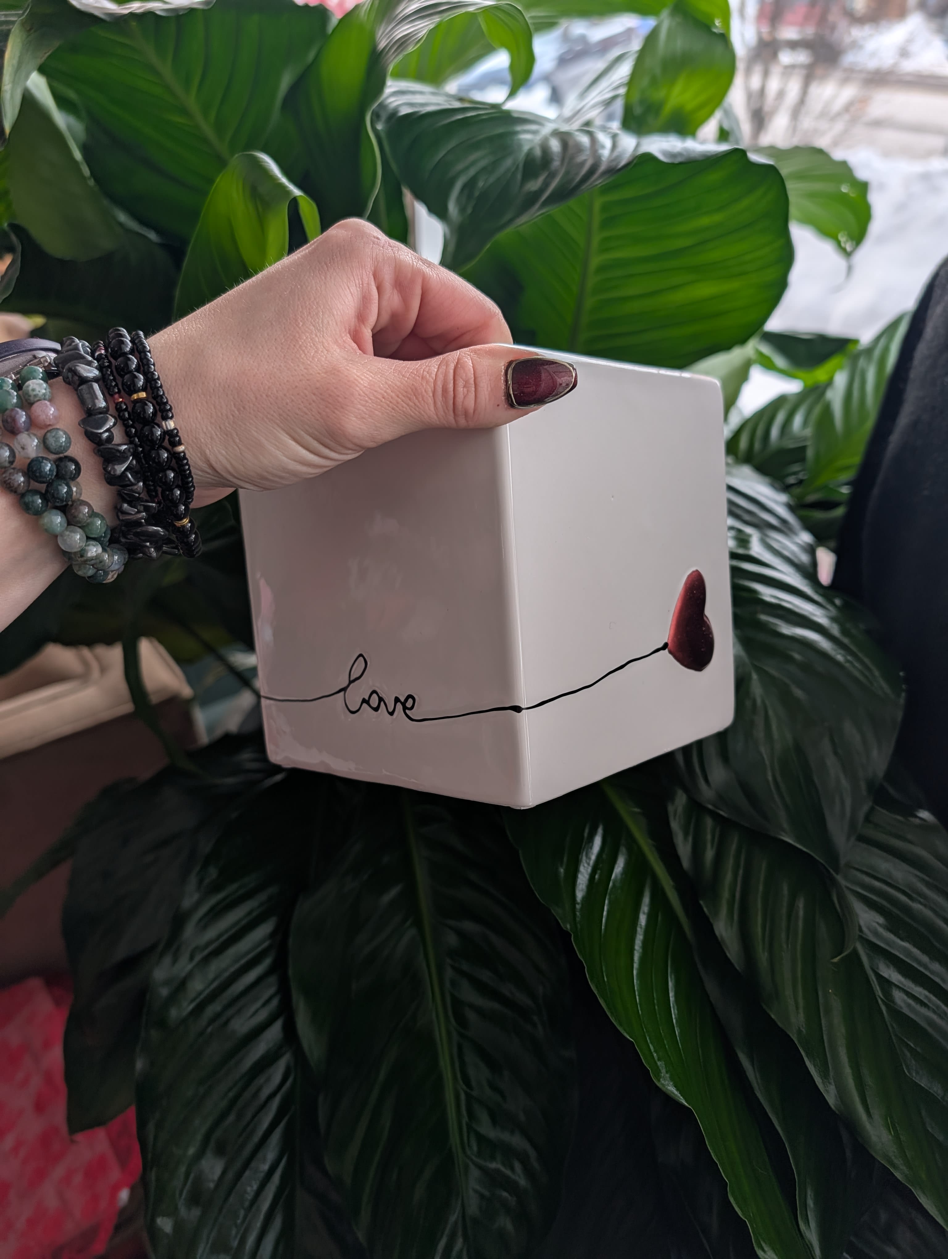 Hand holding a white cube planter in front of large green leaves