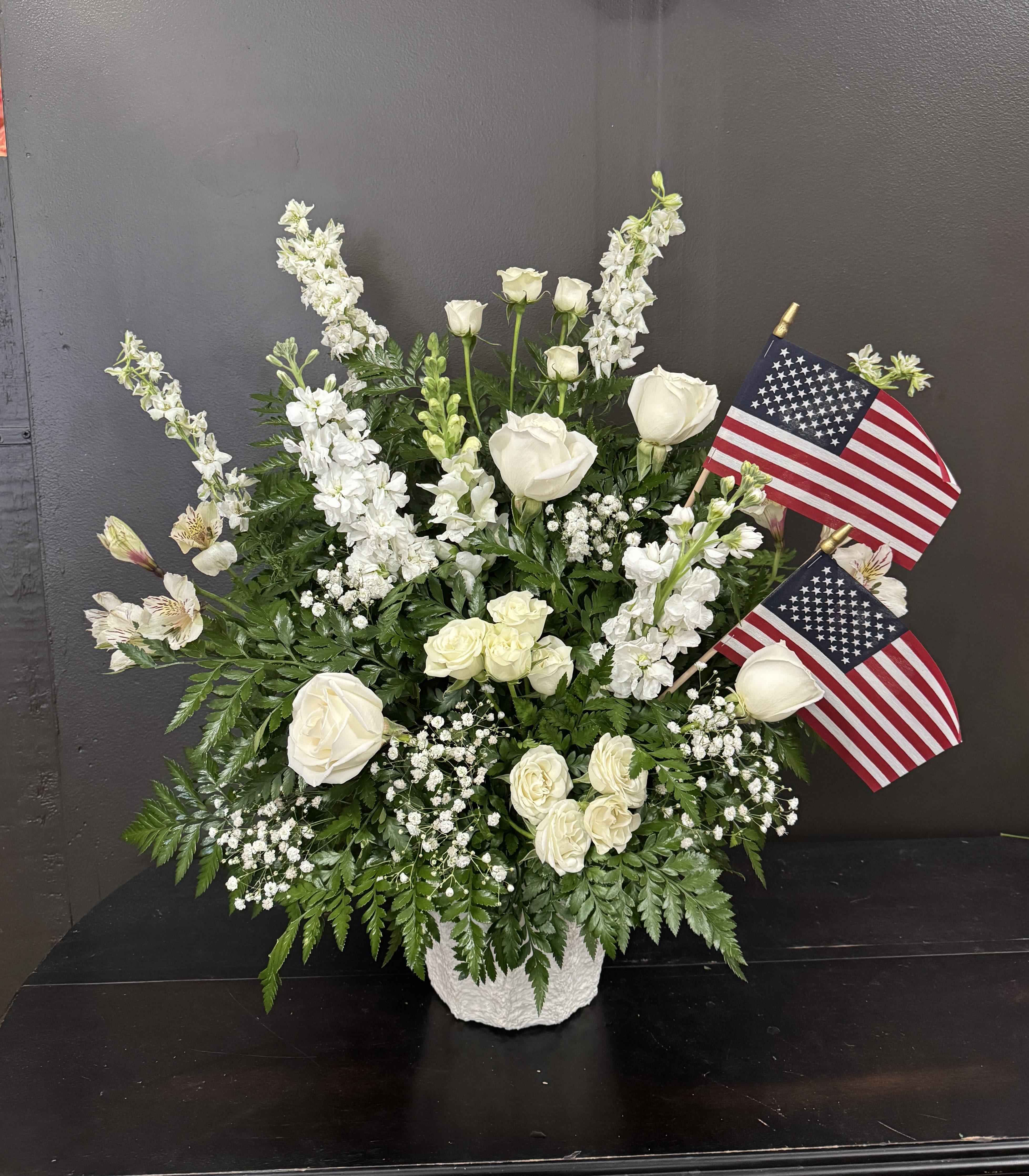 White floral arrangement with two American flags in a white vase