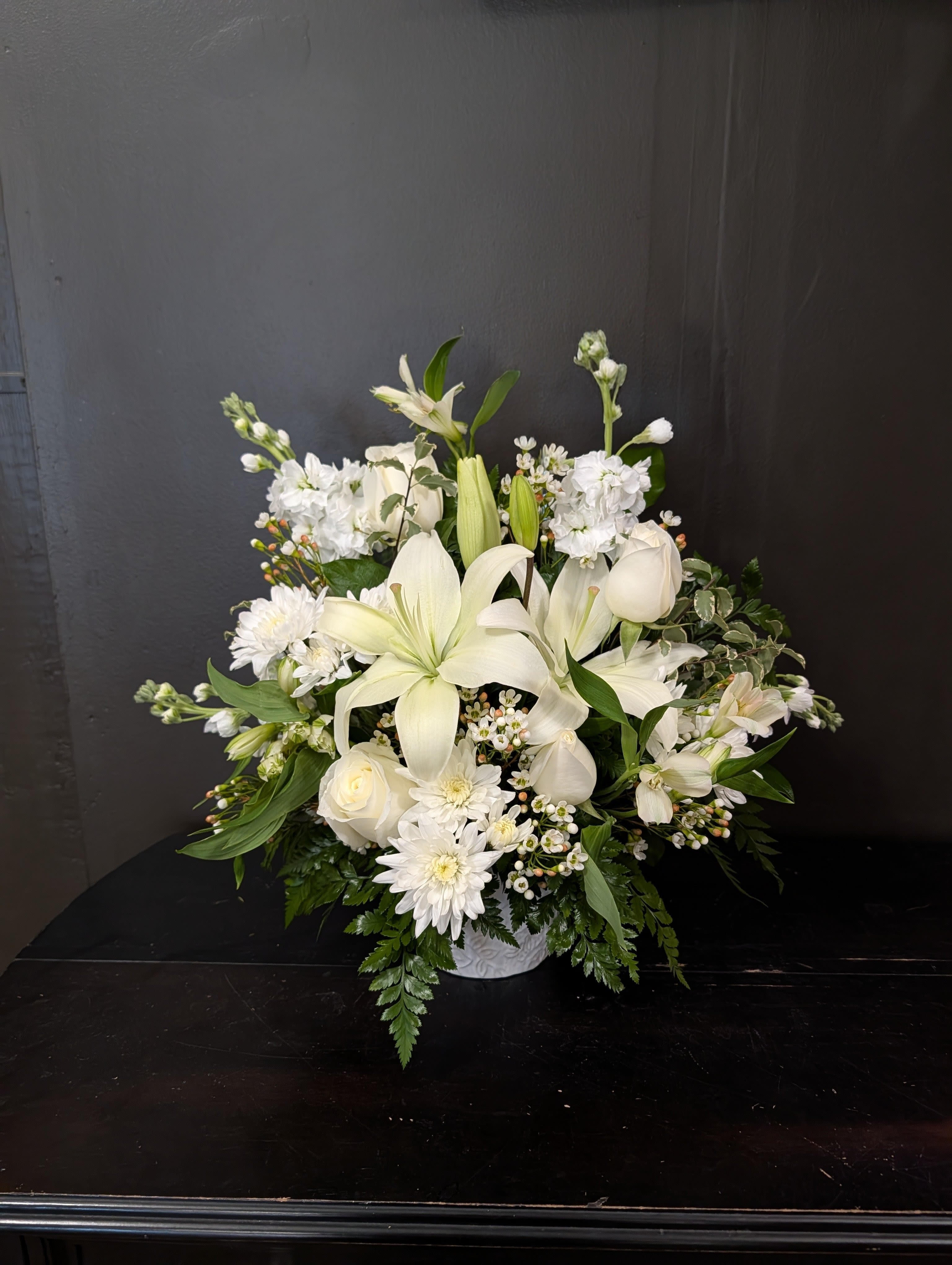 White lilies and roses arranged in a low vase with white daisies