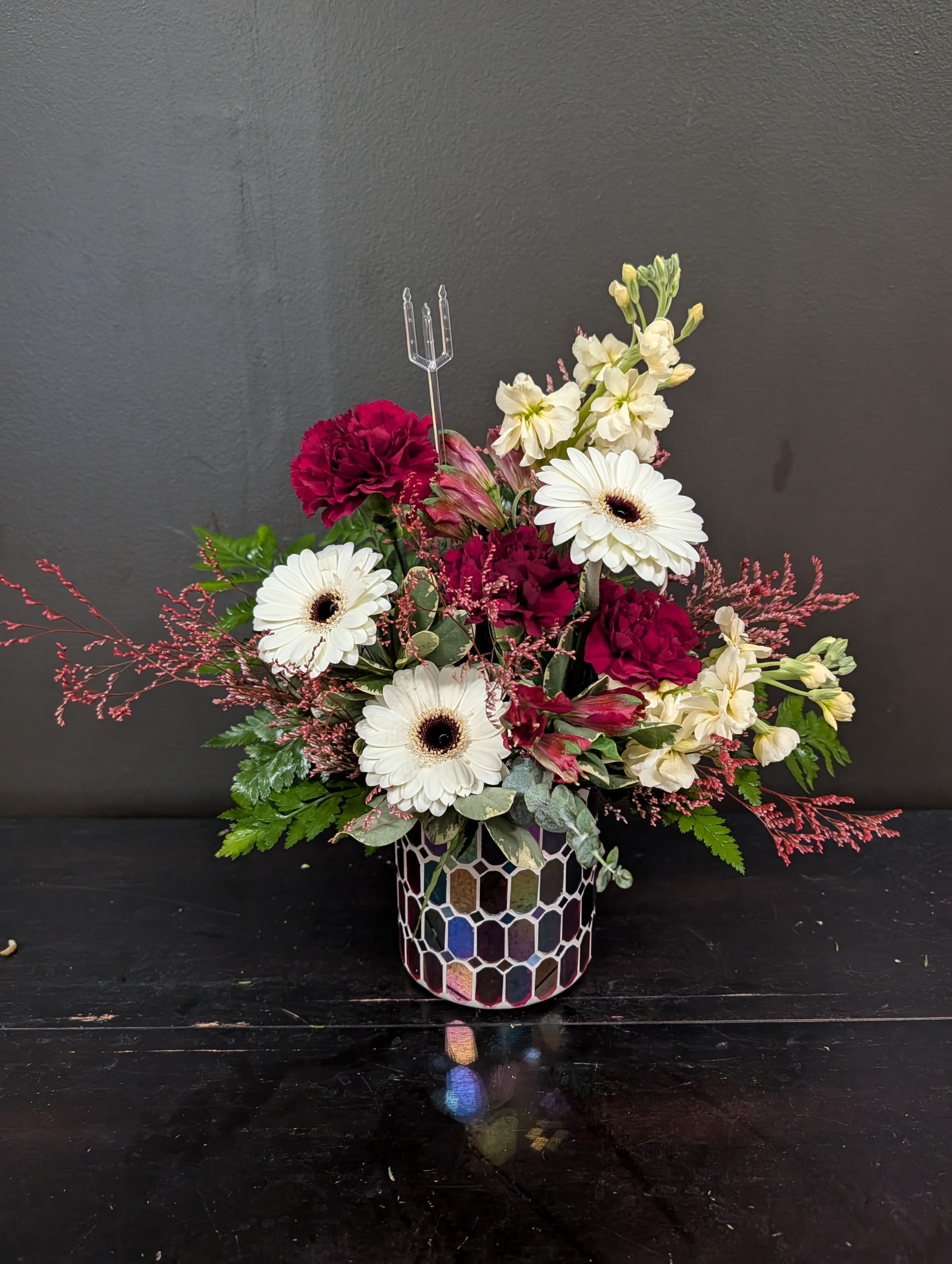 Compact arrangement of red and white flowers in an iridescent mosaic glass vase