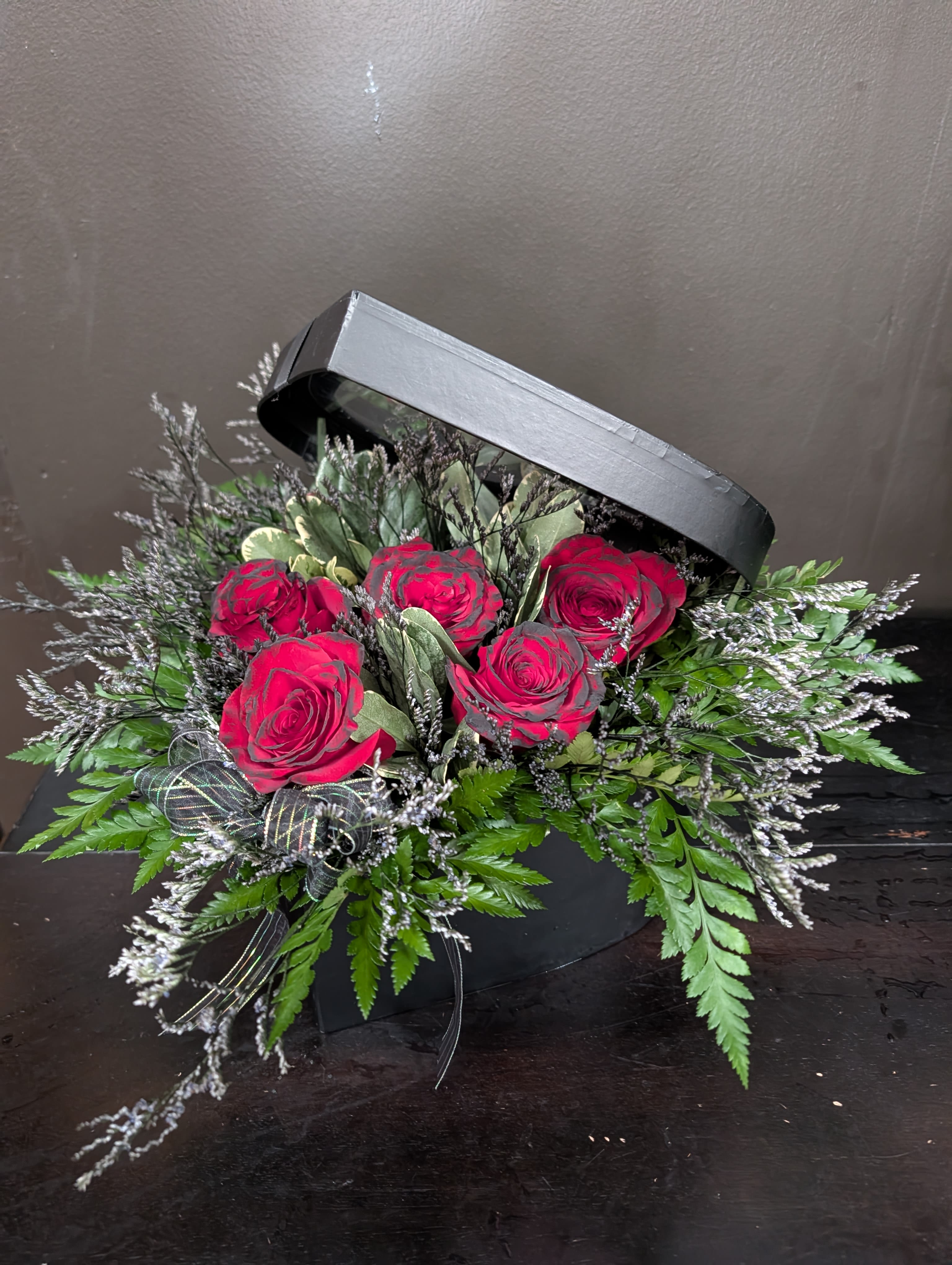 Red roses in a black hatbox with greenery and ribbon