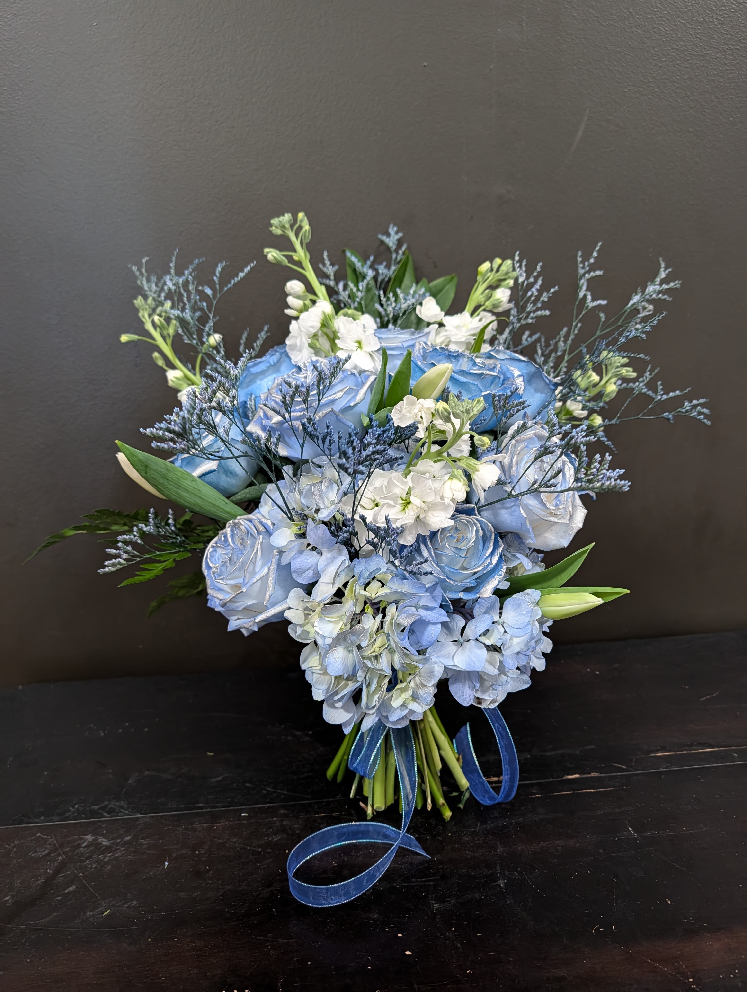 Blue and white bouquet with roses, hydrangeas, and lilies tied with ribbon