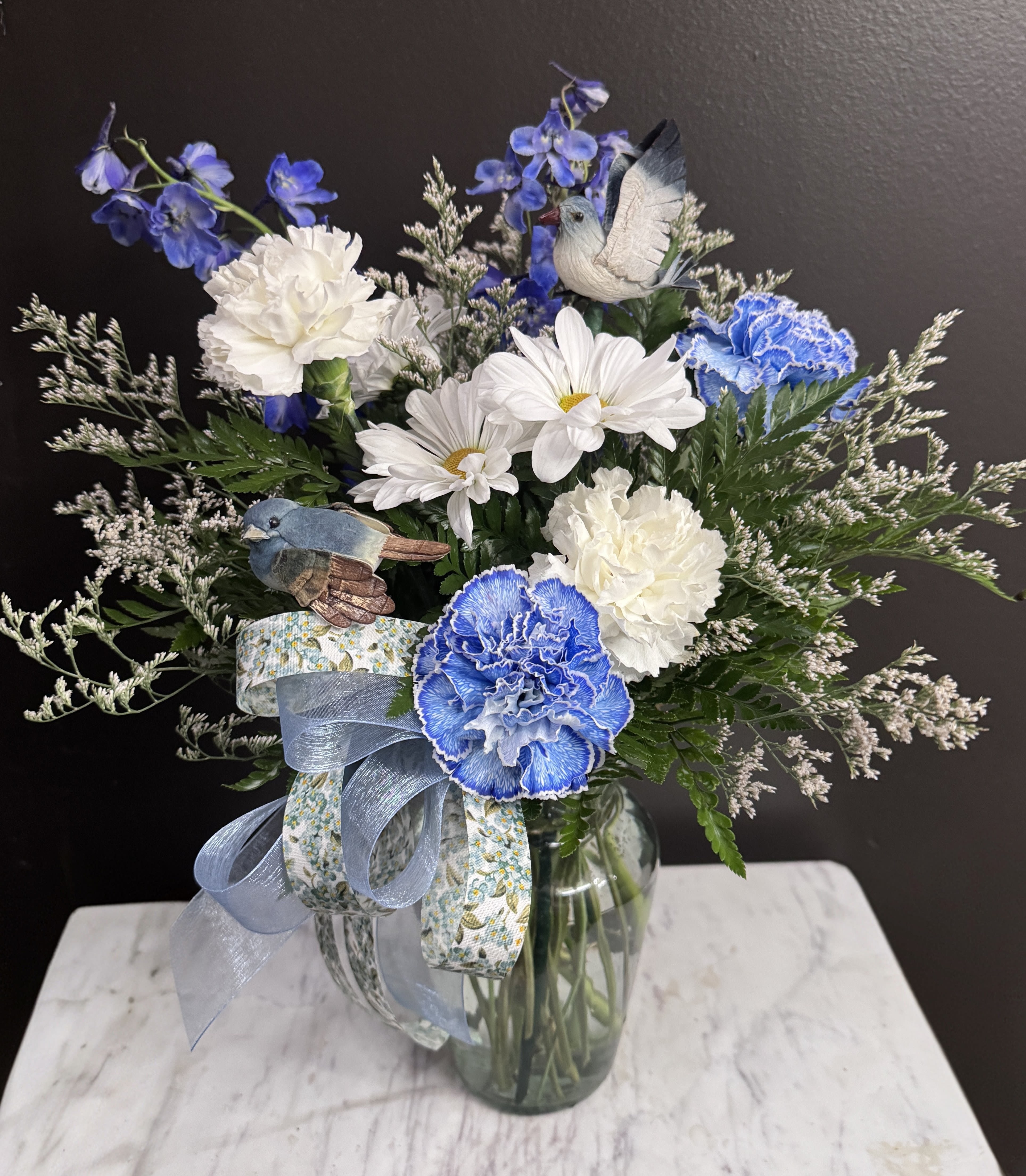 The Blue Bird Special - Blue and white blooms in a clear glass vase accompanied by blue birds. Color of blooms and birds can be changed upon request.