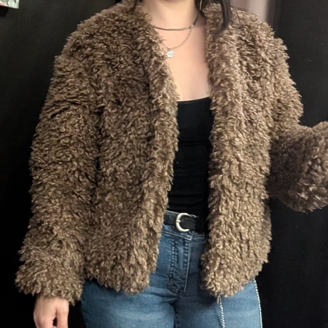 Person wearing a brown shaggy faux-fur jacket over a black top and jeans