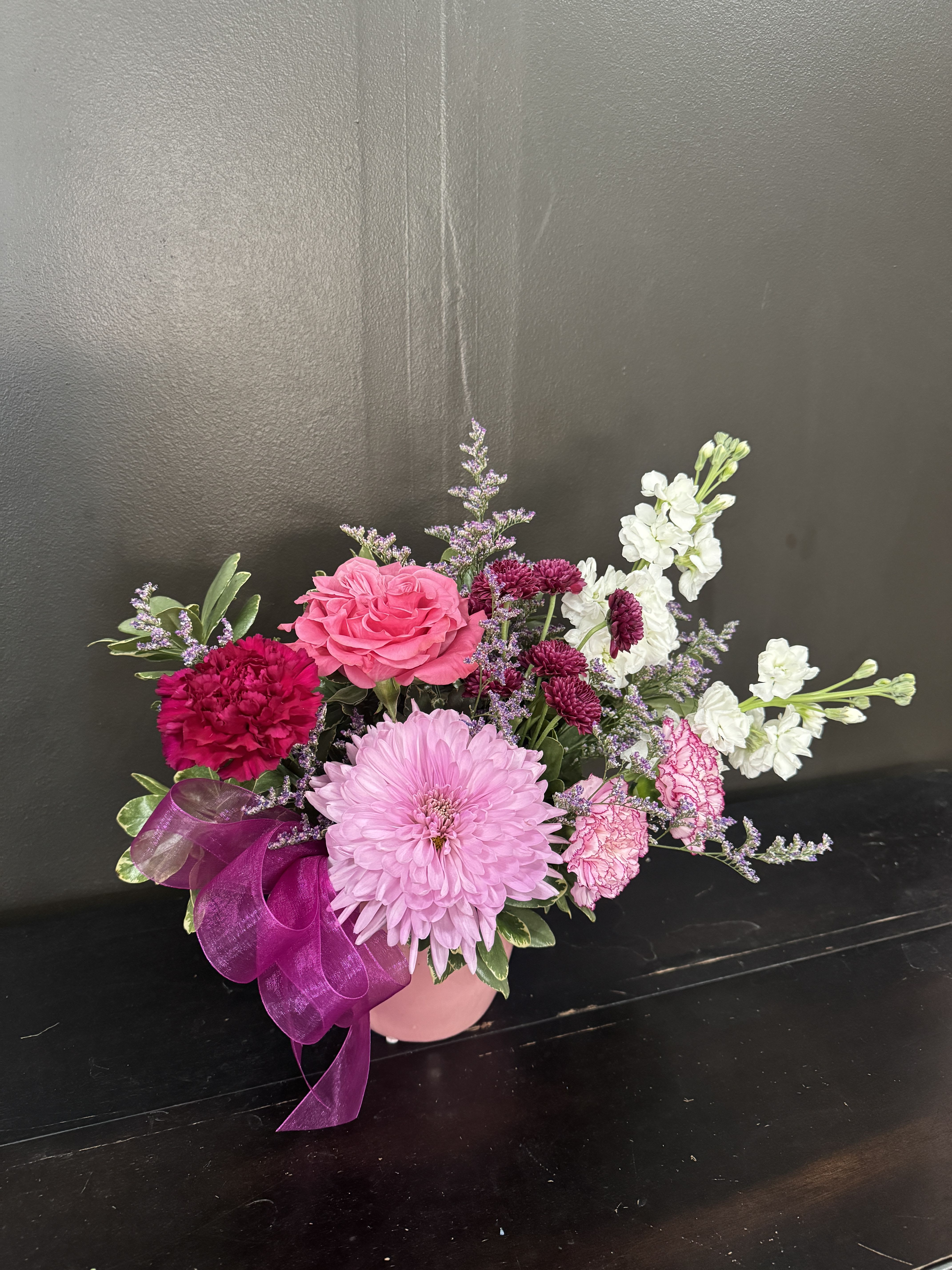 Low pink and white mixed flower arrangement in a pink vase with a purple ribbon bow