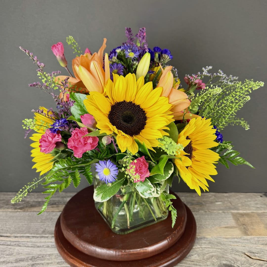 Mixed bouquet with sunflowers, pink blooms, and purple flowers in a glass vase