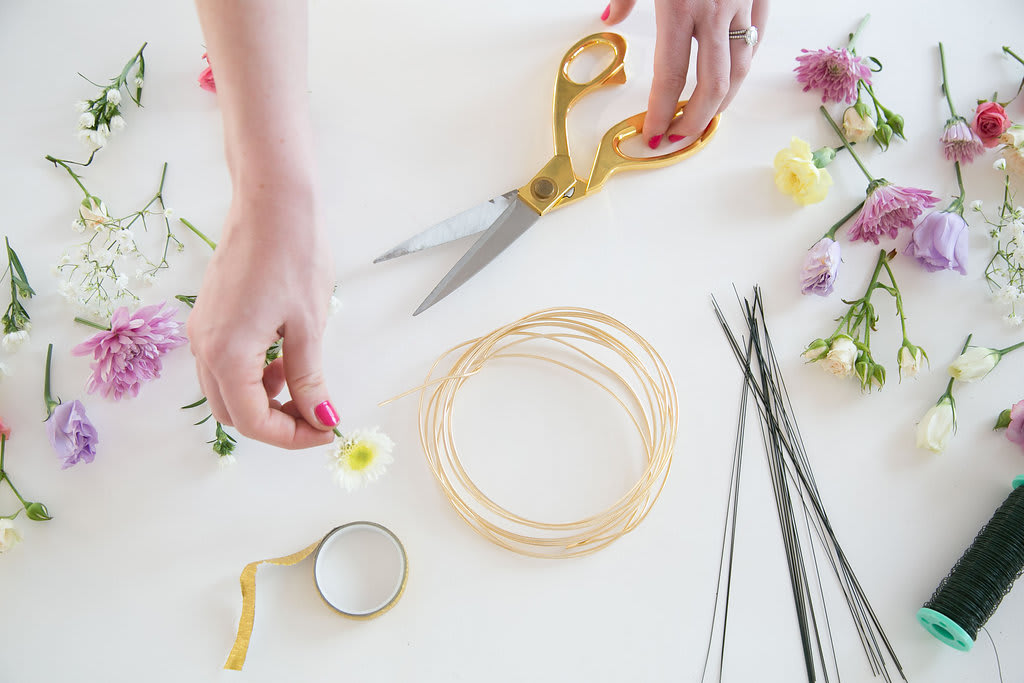 Hands arranging small flowers with scissors and floral wire on a white table