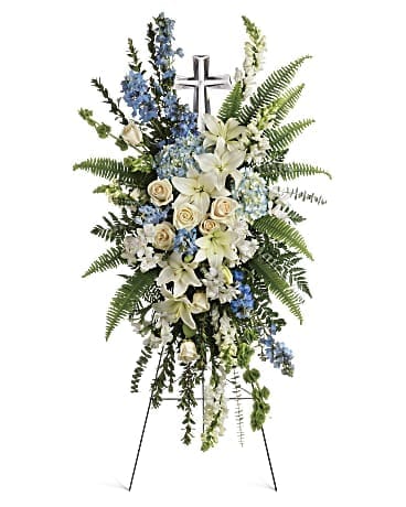 Standing floral spray with white lilies, cream roses, and blue flowers around a cross